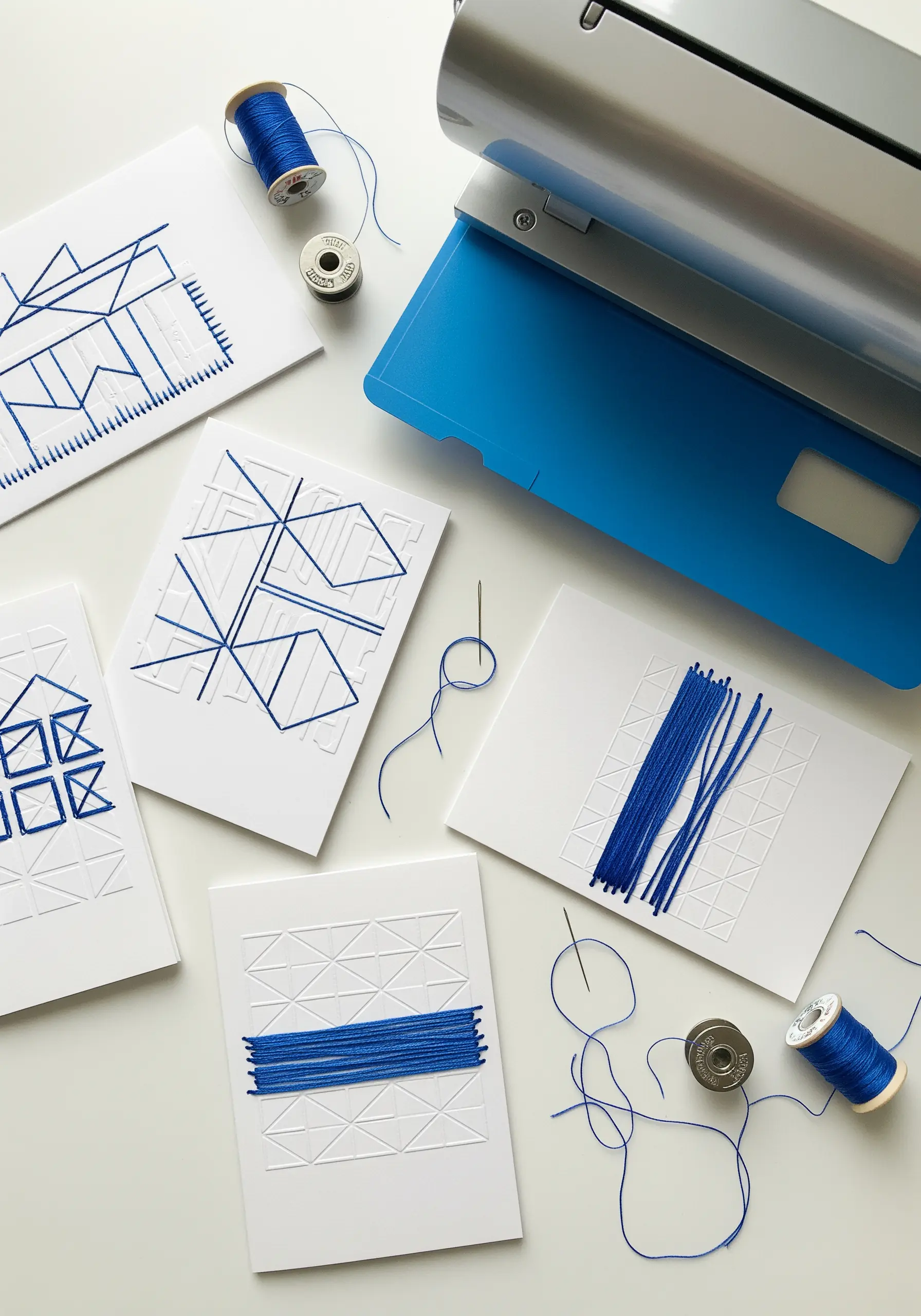 Geometric patterns embossed on white cards, with blue thread stitched to highlight the designs.