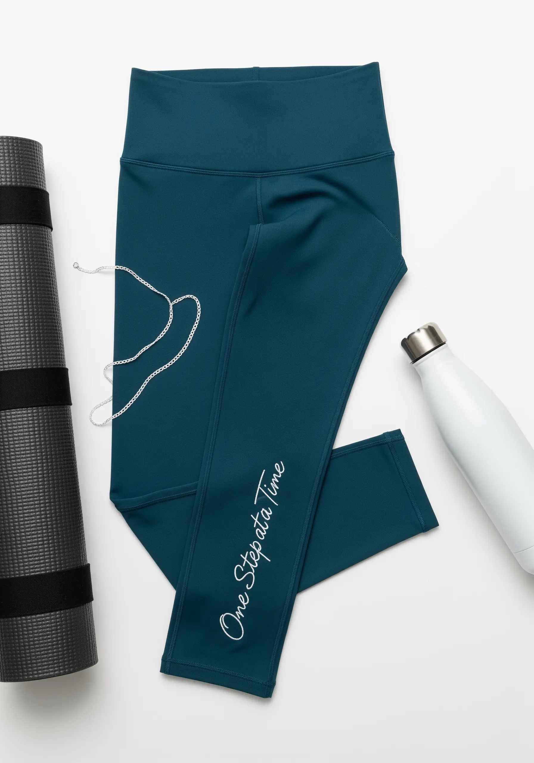 Delicate white script “One Step at a Time” stitched down the calf of teal leggings.