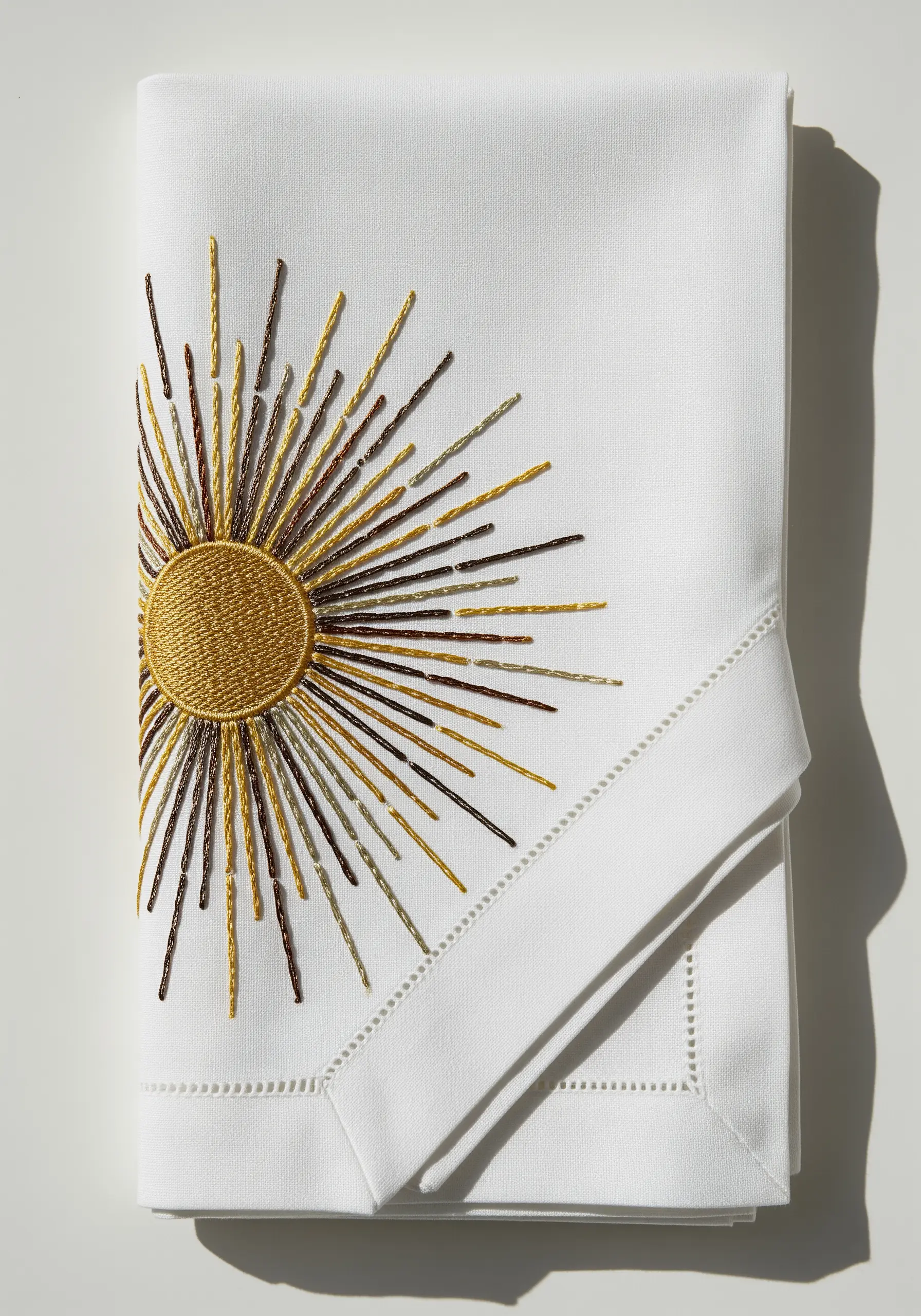 An embroidered sun with a matte gold center and radiating metallic thread rays.
