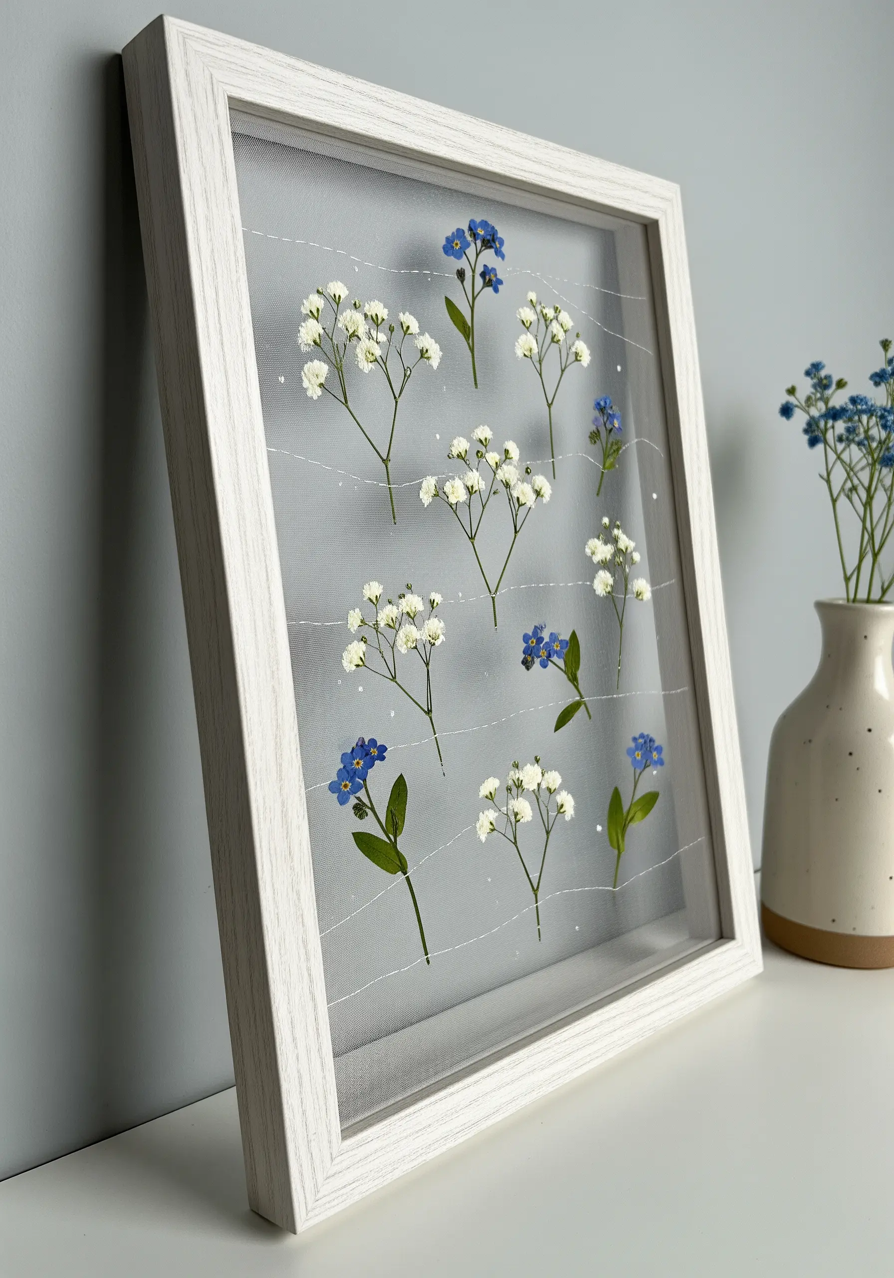 Pressed forget-me-nots and baby's breath stitched onto sheer fabric in a white frame.