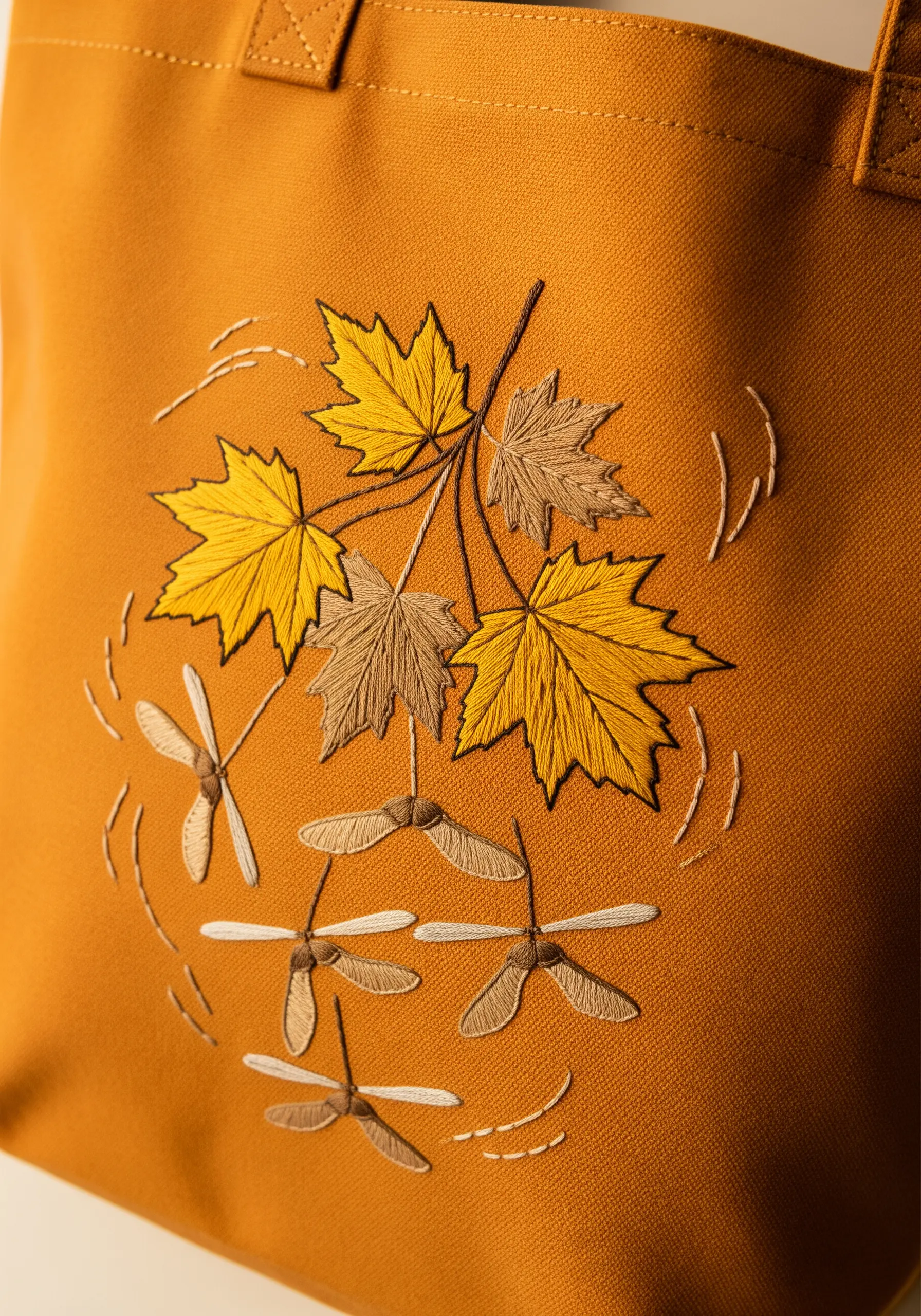 Embroidered maple leaves and seeds swirling on a mustard yellow tote bag.