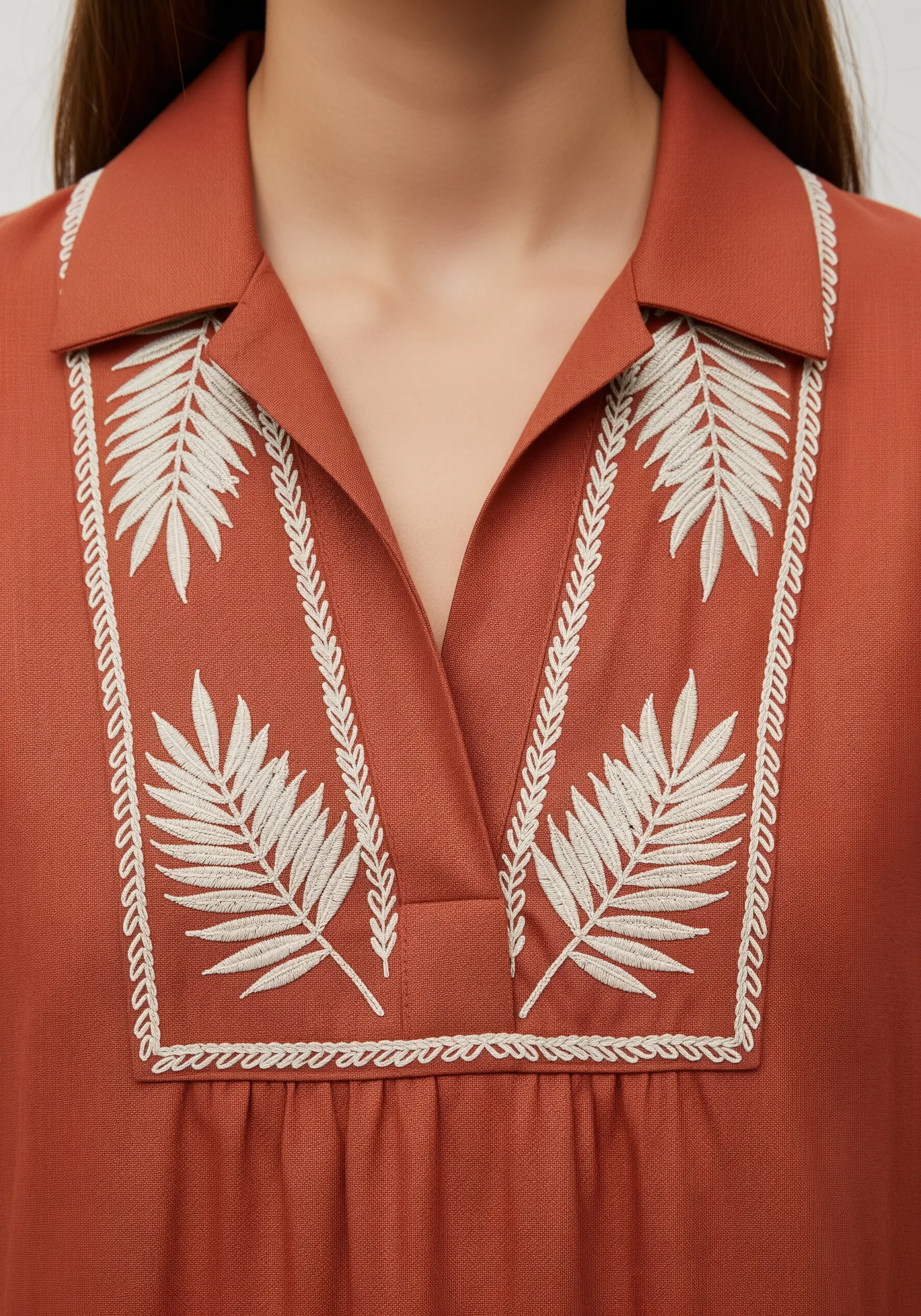 Symmetrical white fern fronds embroidered on either side of the placket of a rust-colored shirt.