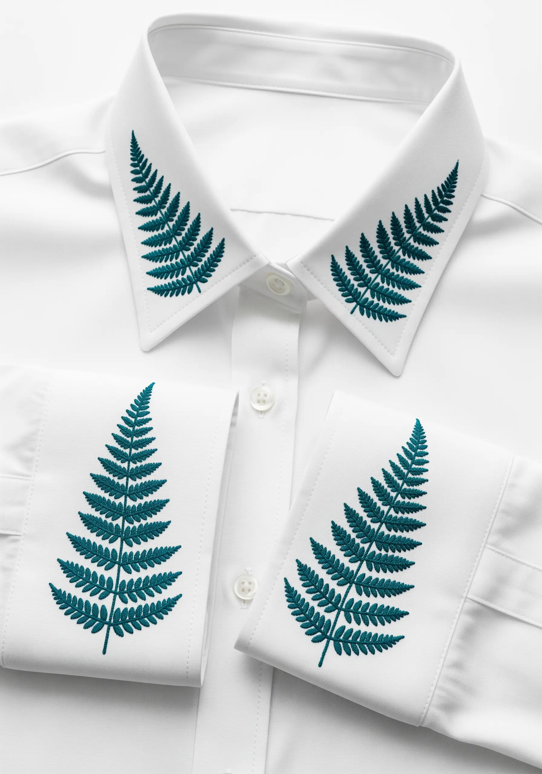 Symmetrical teal-colored fern embroidery on the collar points and cuffs of a white dress shirt.