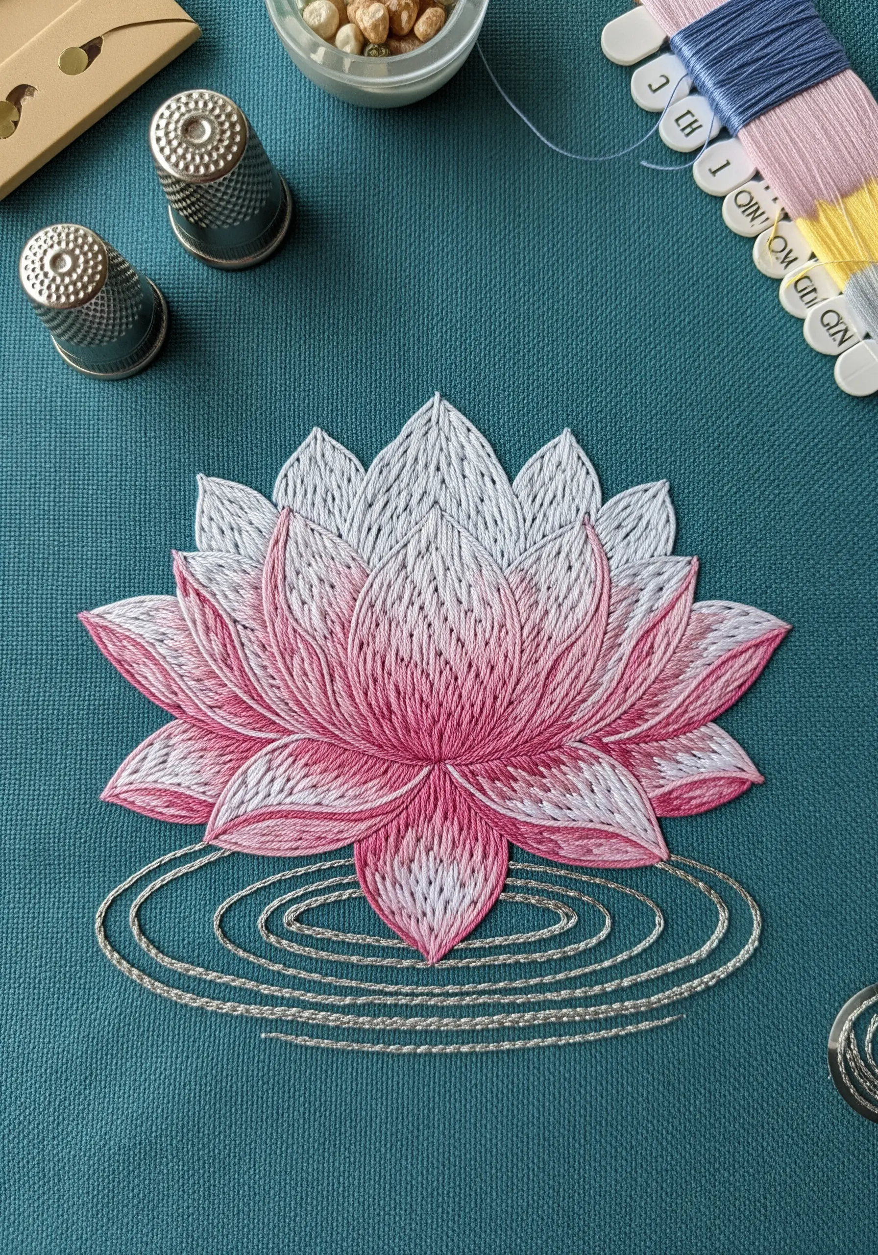 Pink and white lotus flower embroidery on teal fabric with silver water ripples