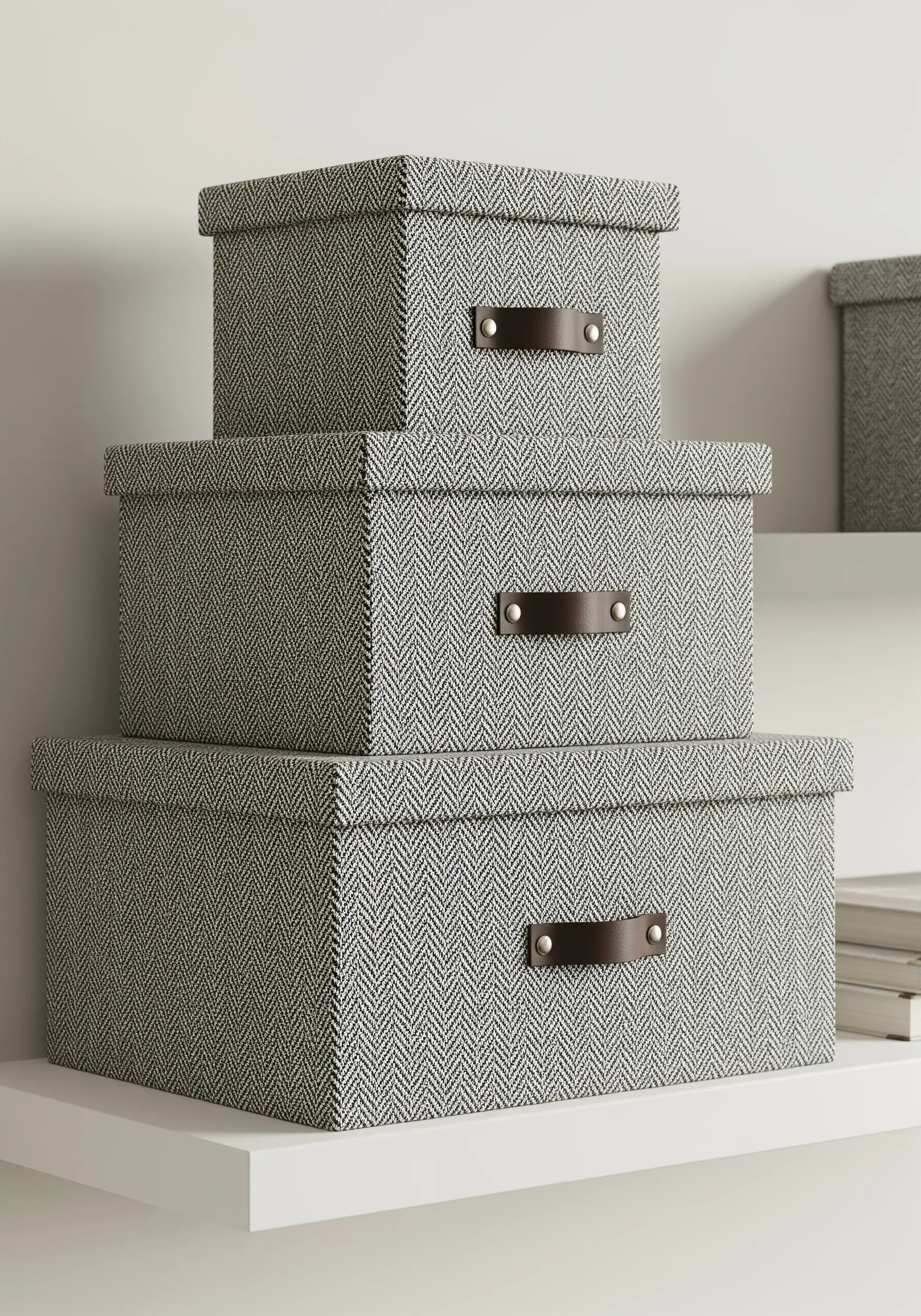 A stack of three rectangular storage boxes covered in a gray herringbone fabric.