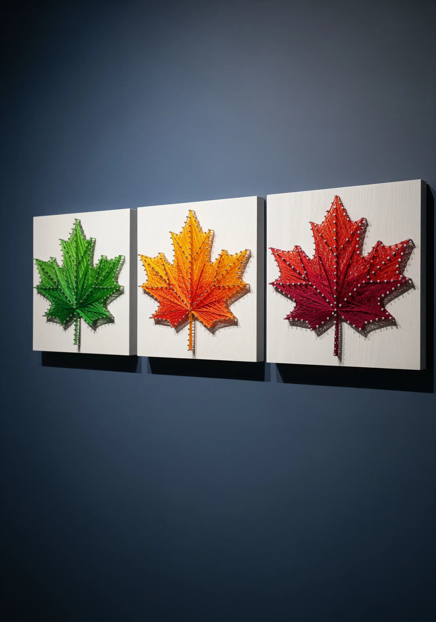 A triptych of three string art maple leaves in green, orange, and red.