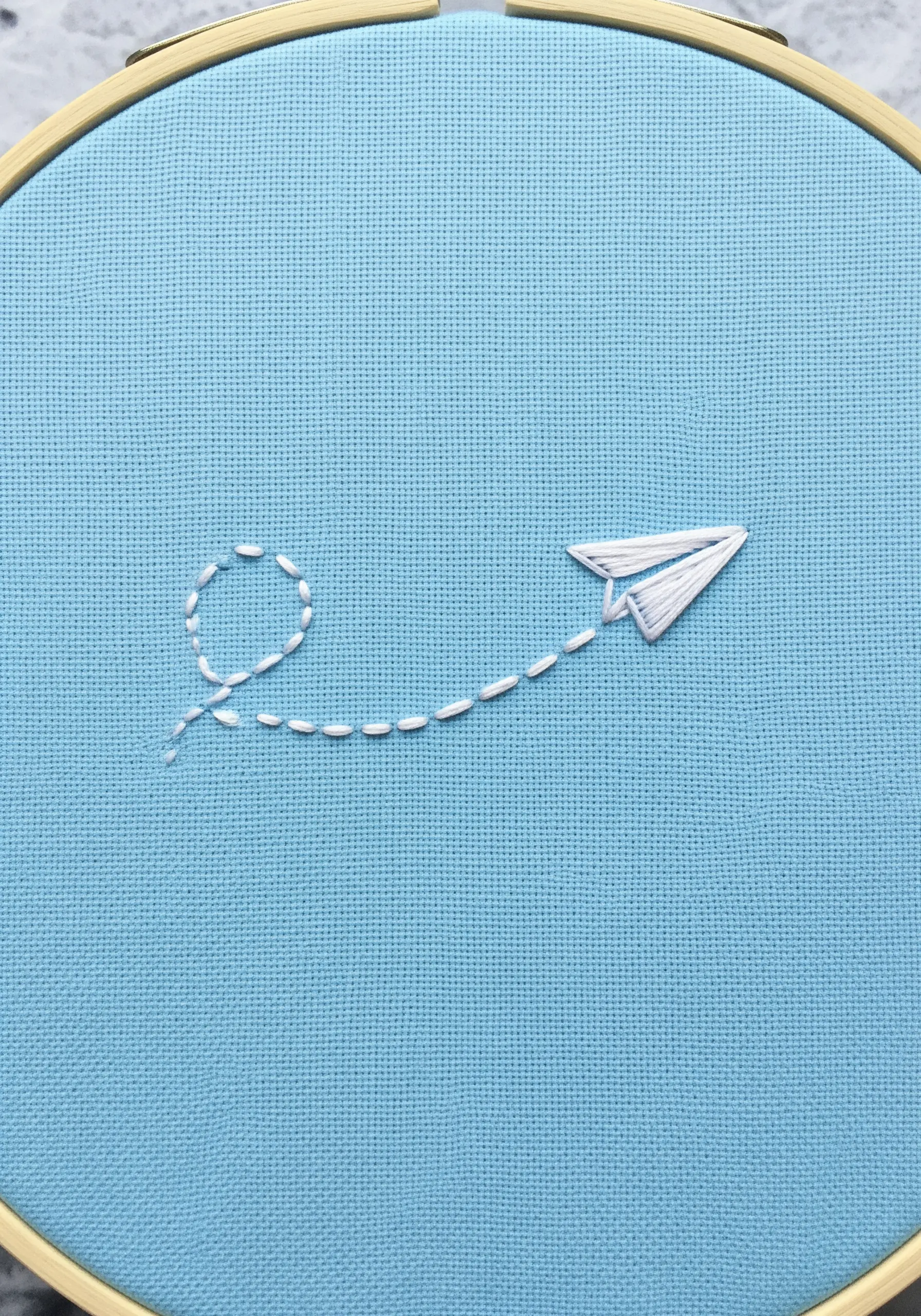 A paper airplane with a dashed line flight path embroidered in white.