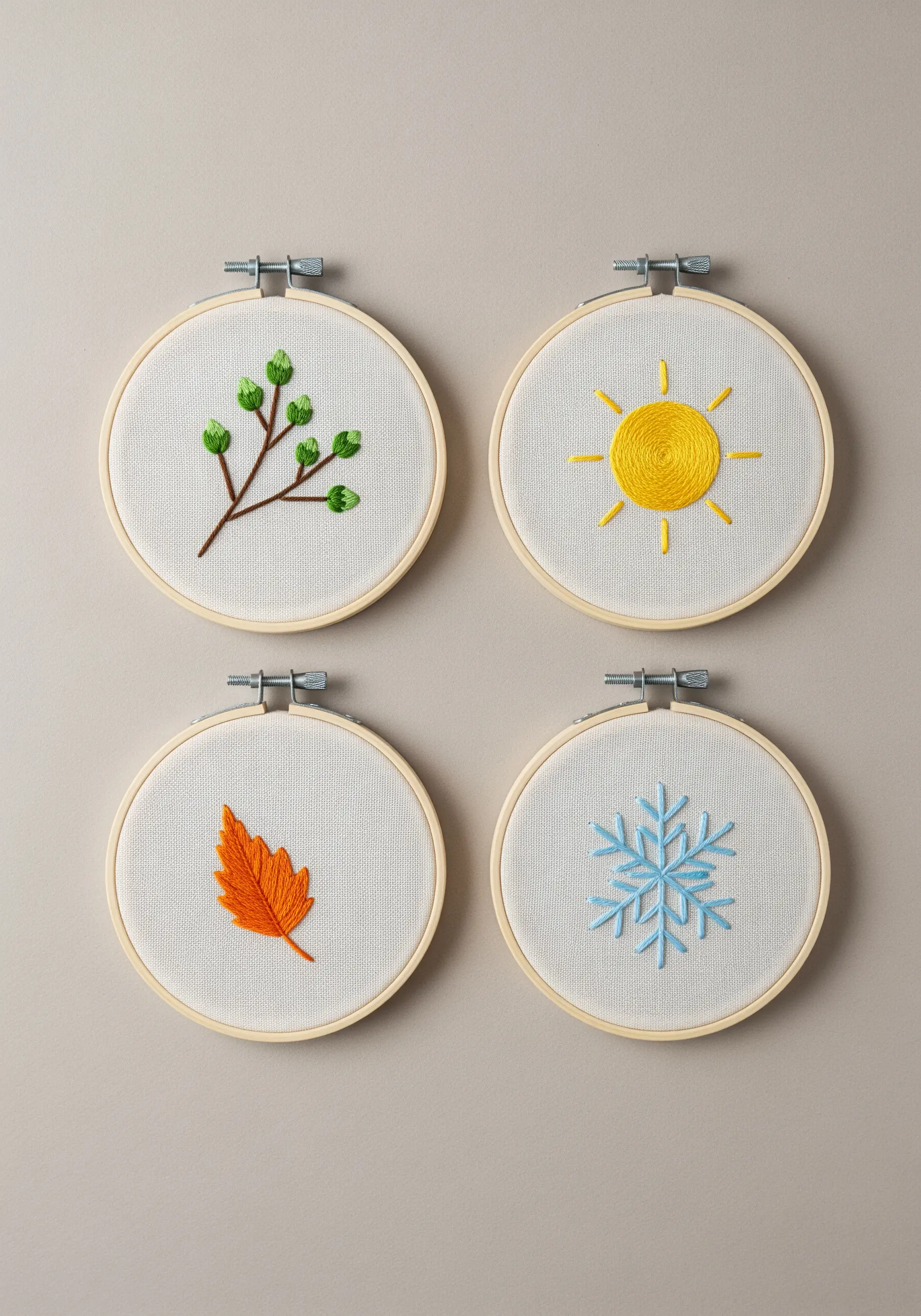 Four small embroidery hoops, each depicting a simple icon for one of the four seasons.