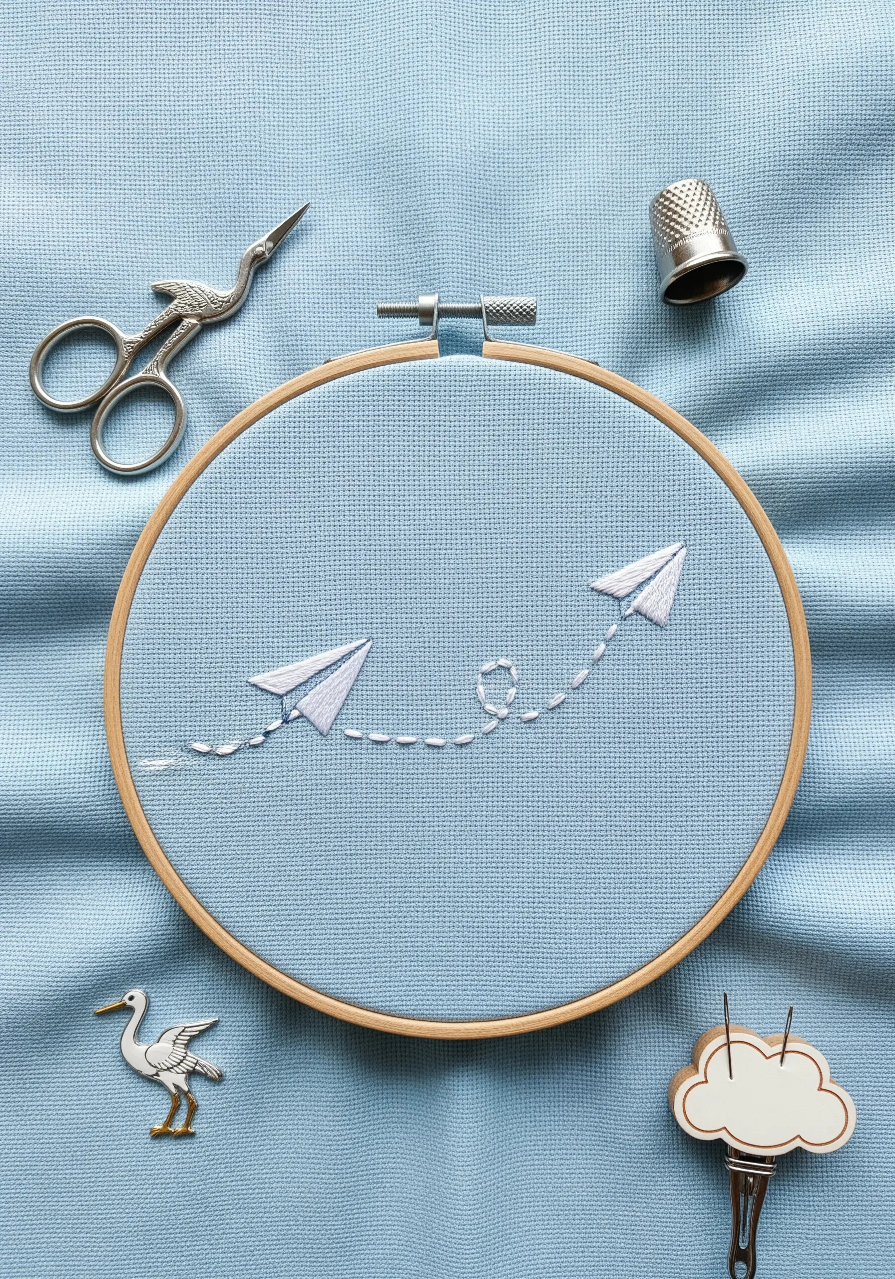 Two paper airplanes stitched in white, connected by a dashed-line flight path on blue fabric.