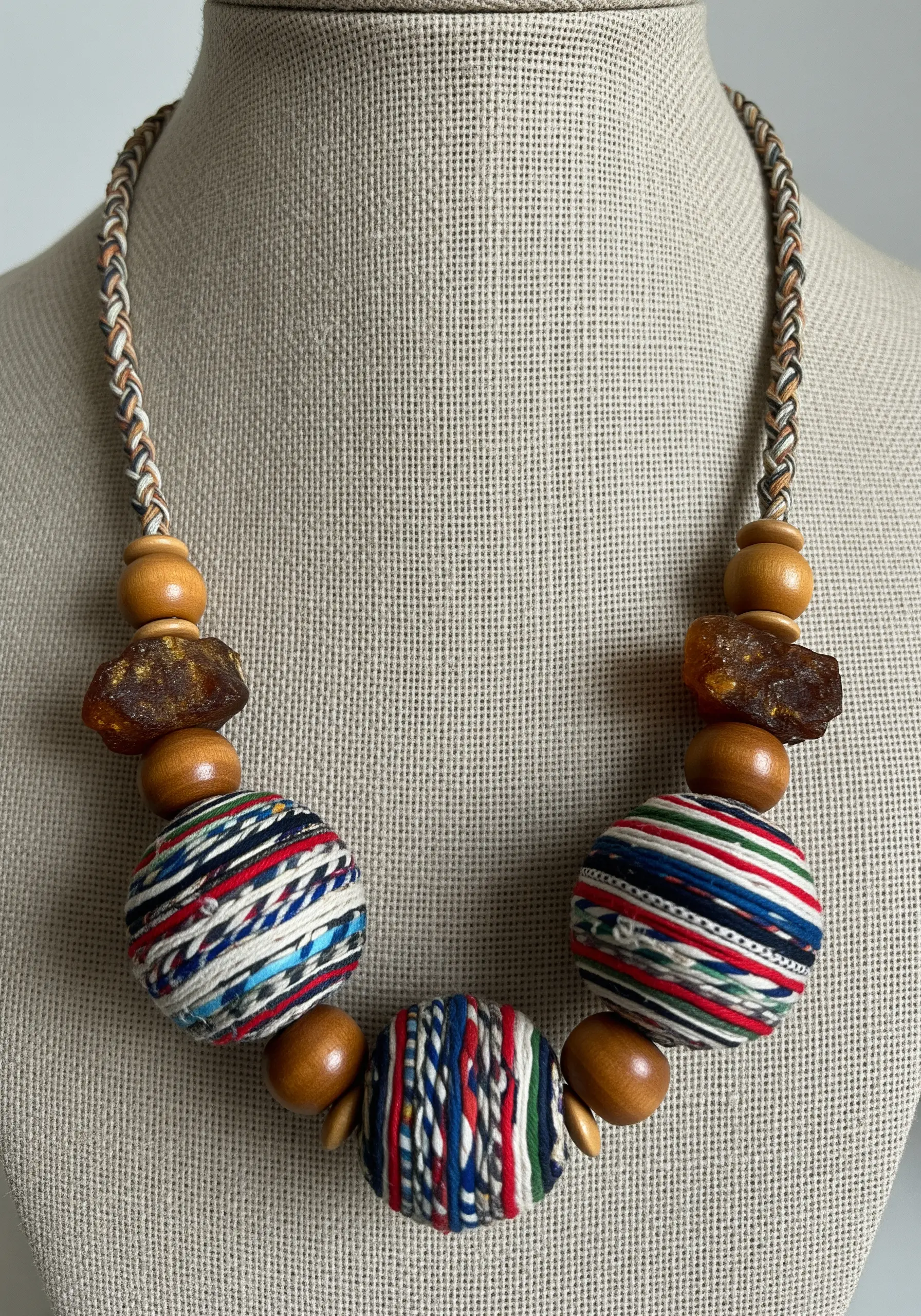 A necklace made with large beads wrapped in colorful striped fabric and wooden beads.