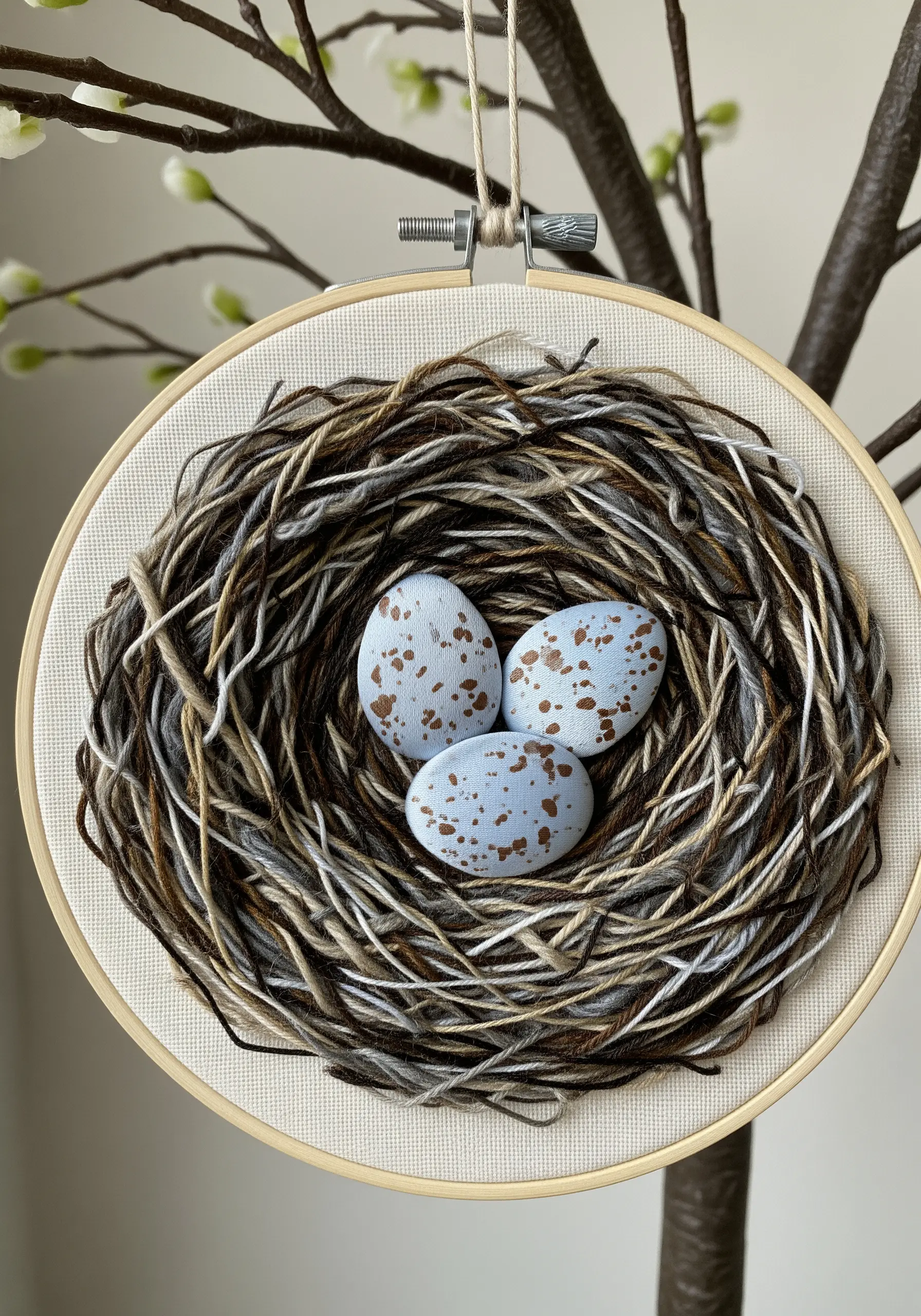 A mixed-fiber embroidery of a bird's nest with three speckled eggs inside.