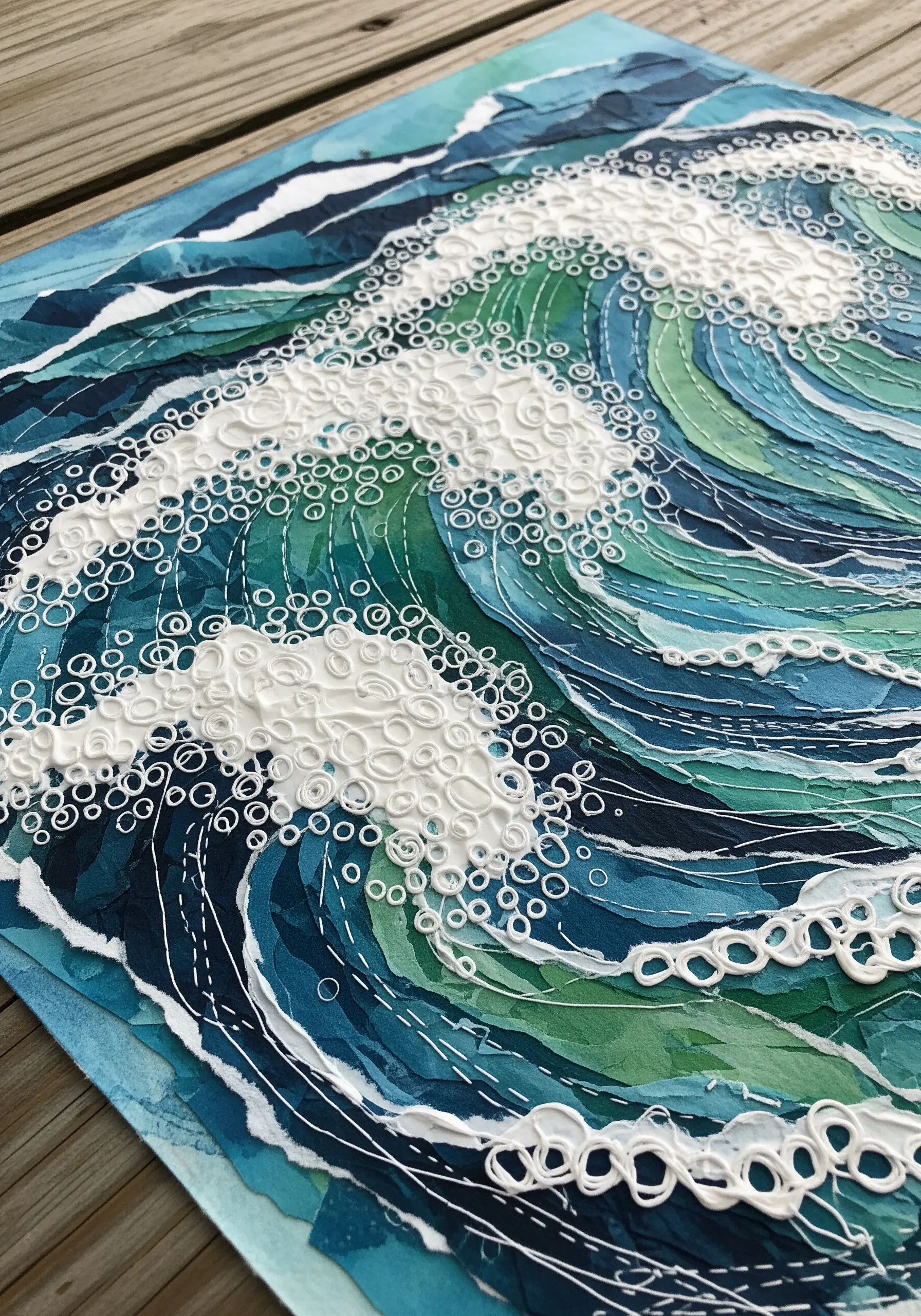 A paper collage ocean wave with dimensional white embroidery creating sea foam texture.