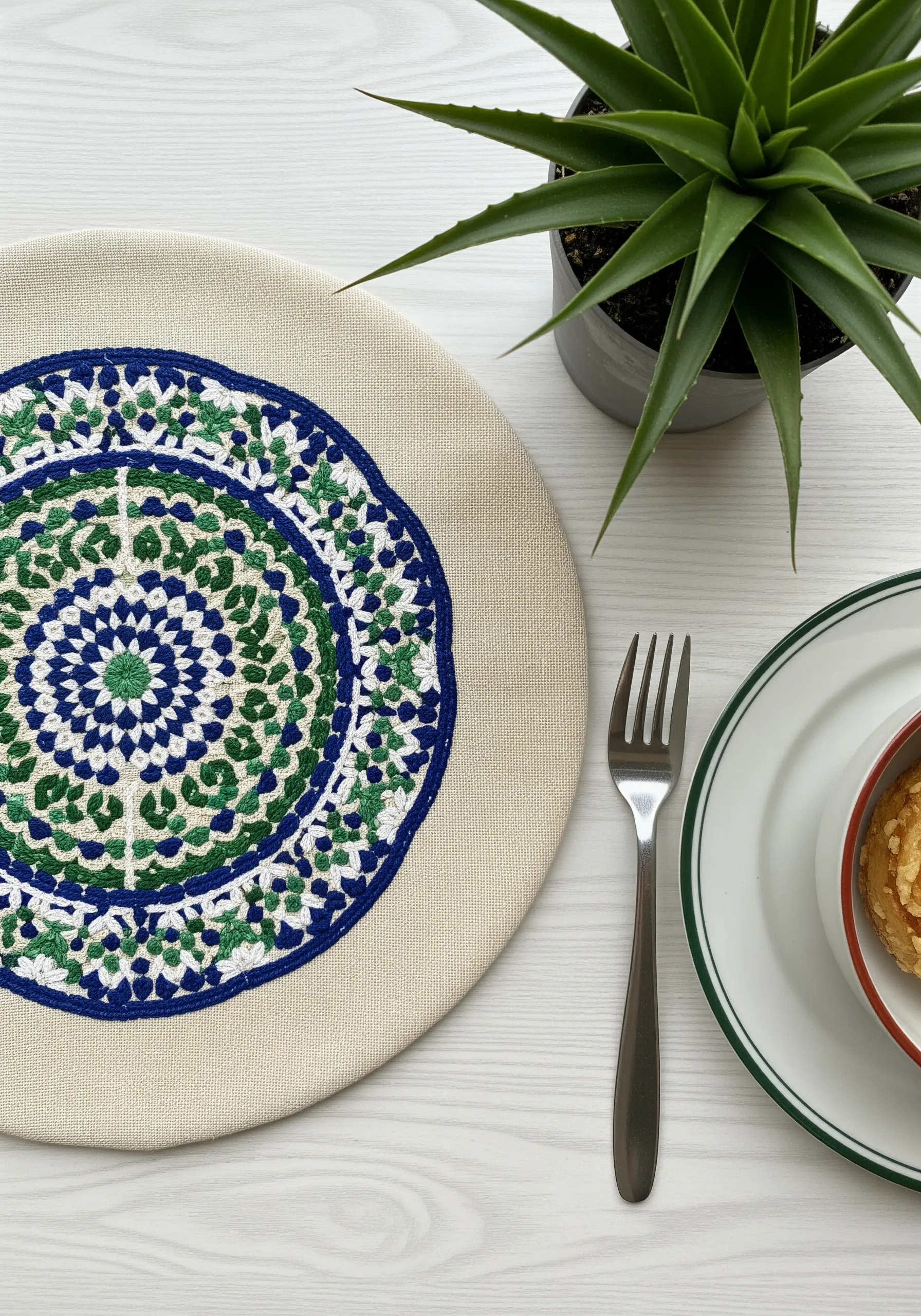 A round placemat with an embroidered mosaic mandala in blue, green, and white.