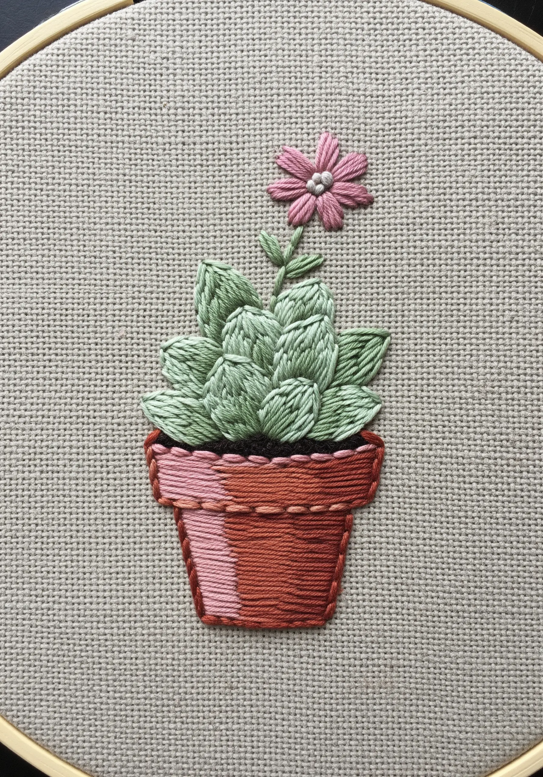 An embroidered succulent in a terracotta pot using layered short stitches for texture.