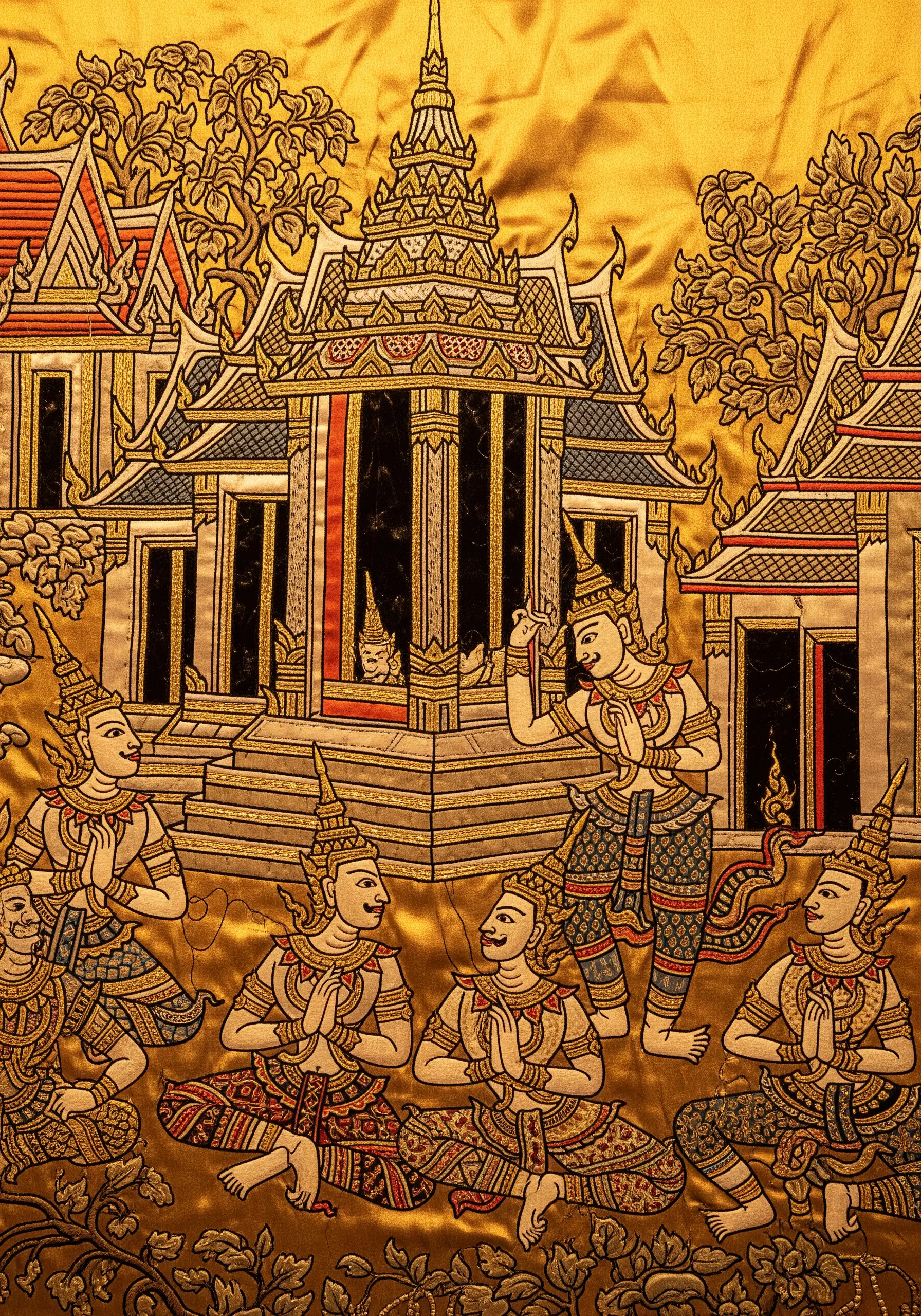 An embroidered Thai temple mural with detailed figures outlined in black and gold.