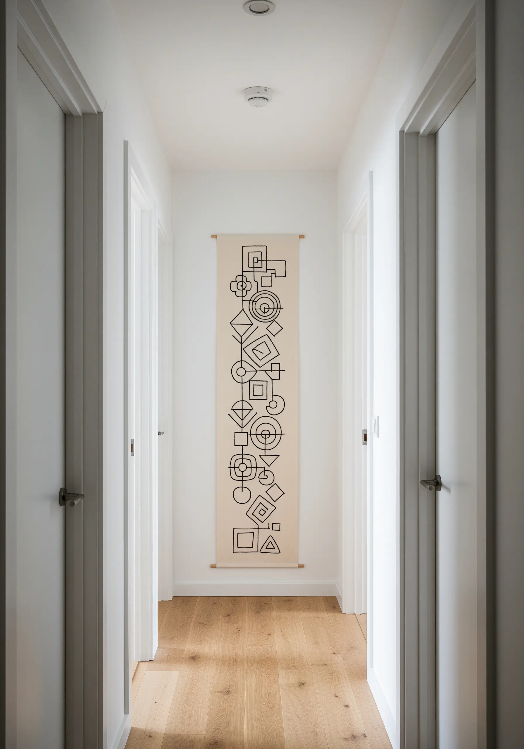 A long, narrow wall hanging with interconnected abstract geometric shapes embroidered in black.