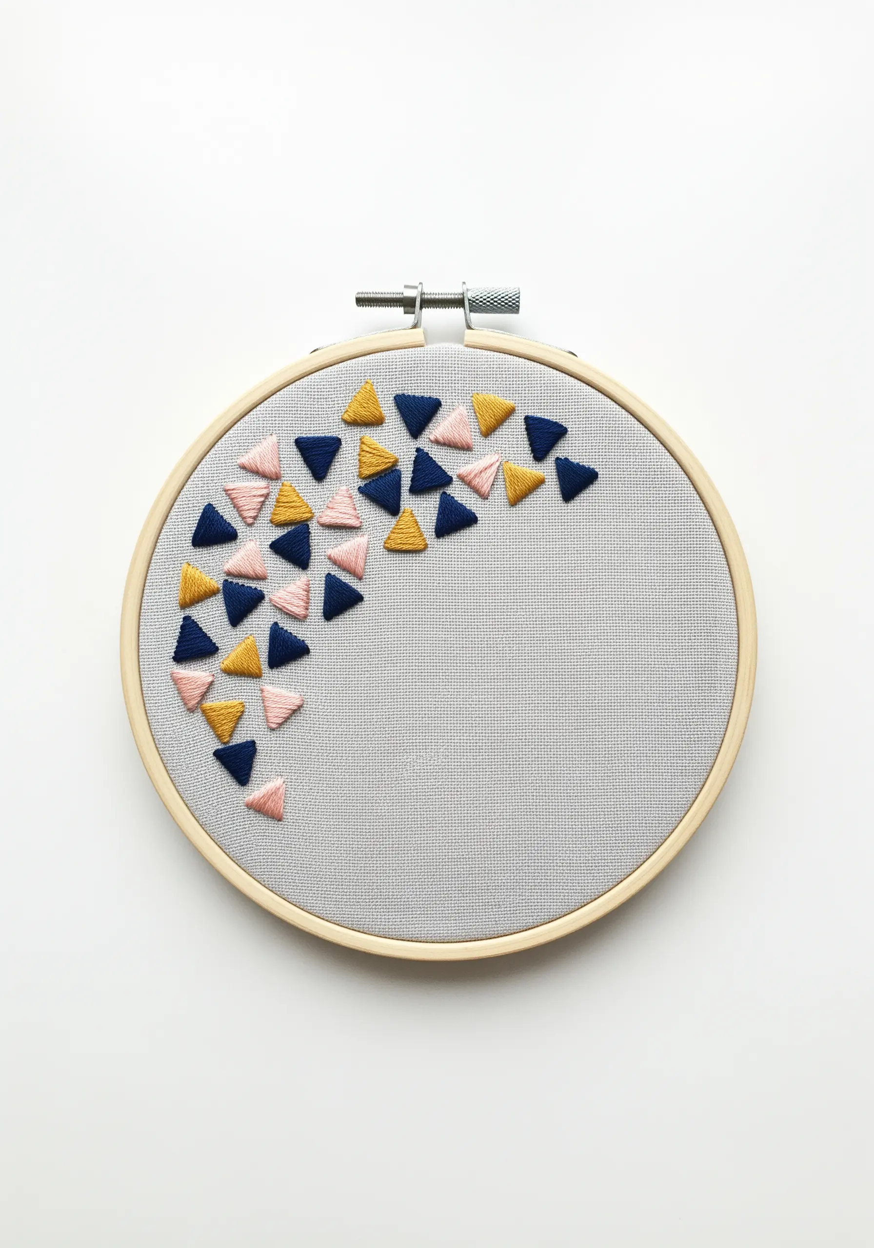 Scattered navy, pink, and yellow satin-stitched triangles on grey fabric.