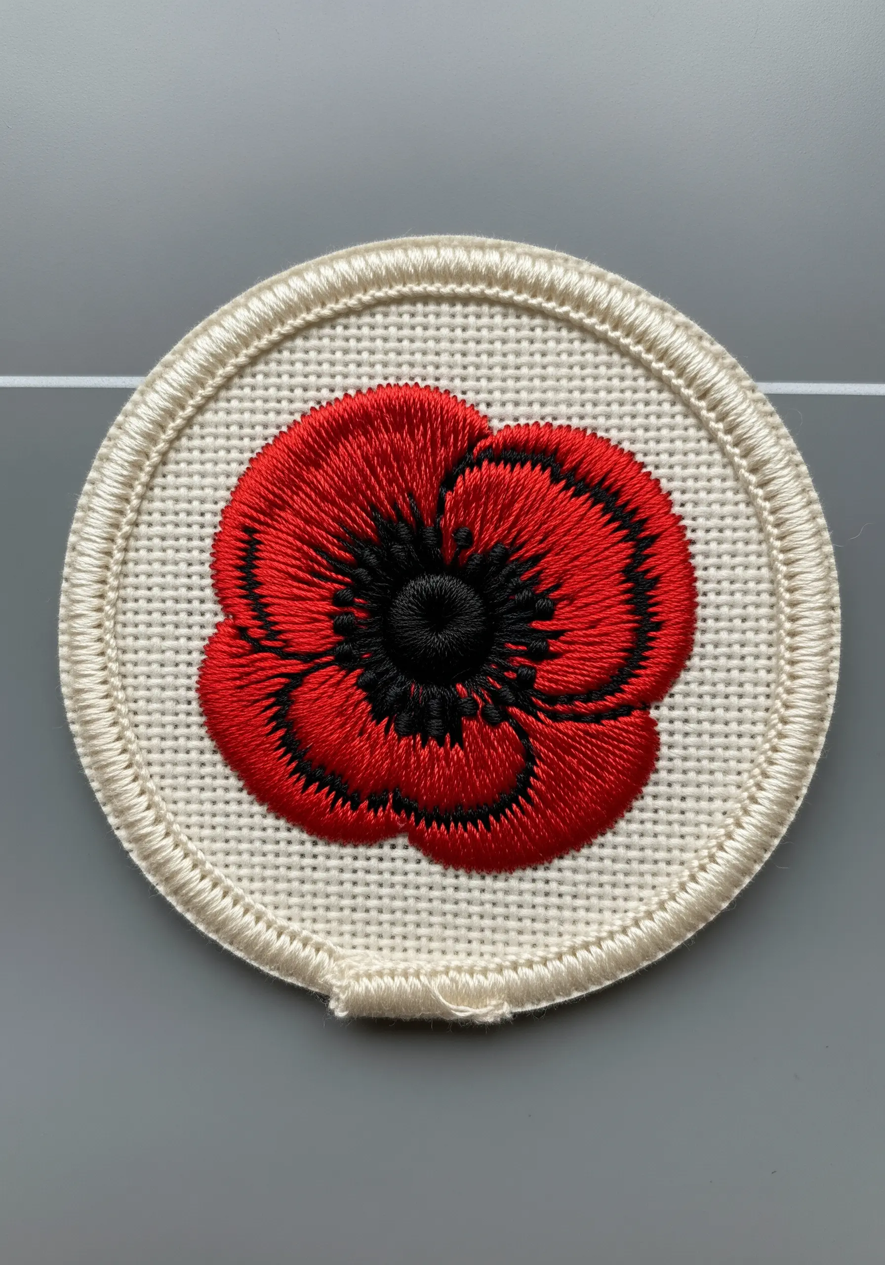 A high-contrast red poppy embroidery patch with black satin stitch details and outline.