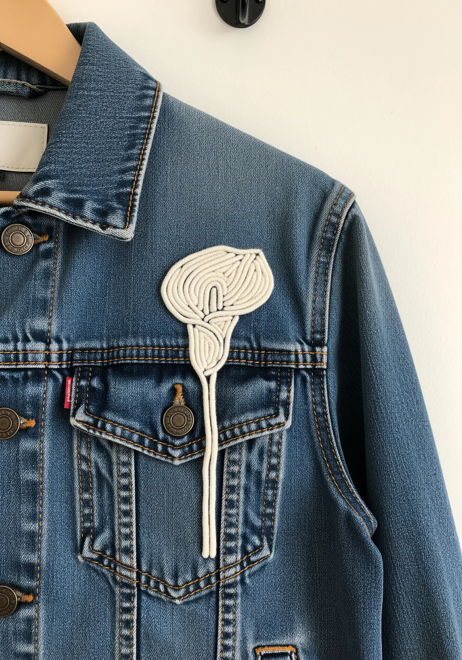 A three-dimensional calla lily patch made with white cord, attached to a denim jacket.