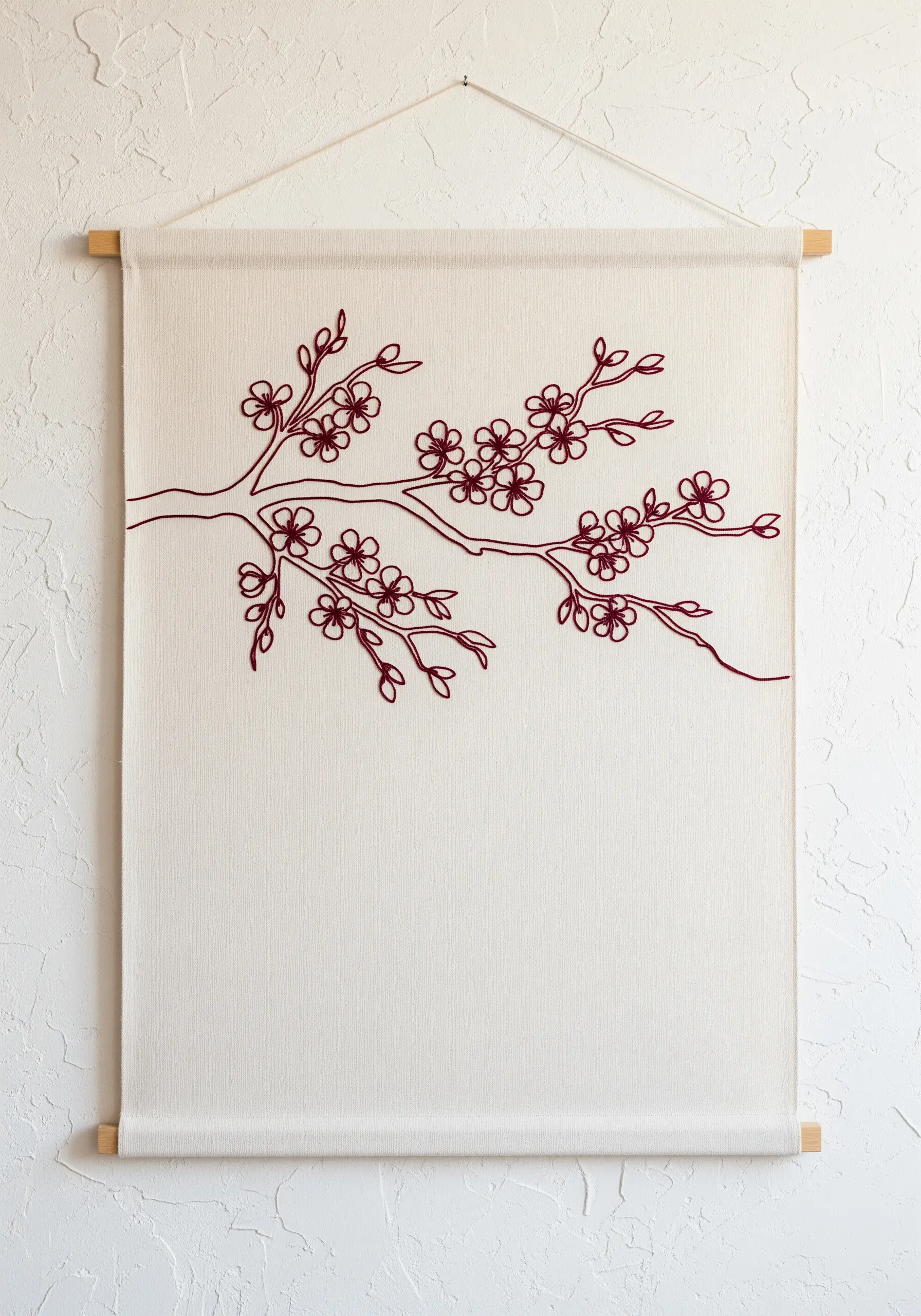 Burgundy one-line cherry blossom branch embroidered on a large neutral wall hanging.