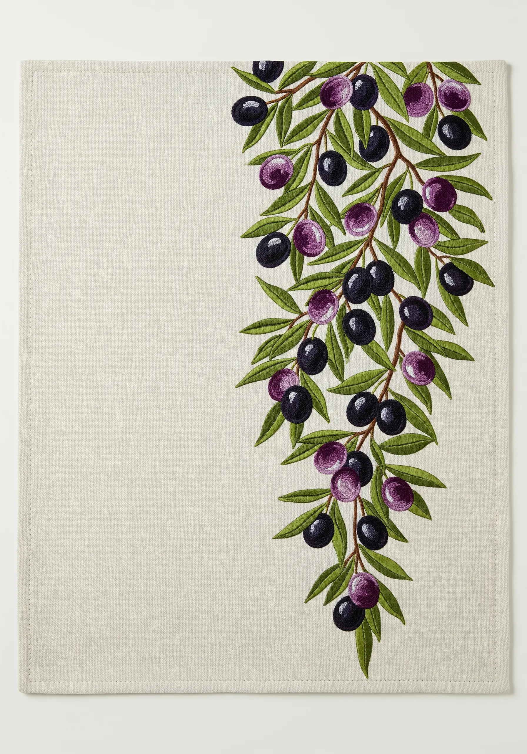 Close-up of a cascading olive branch embroidered on the corner of a linen placemat.
