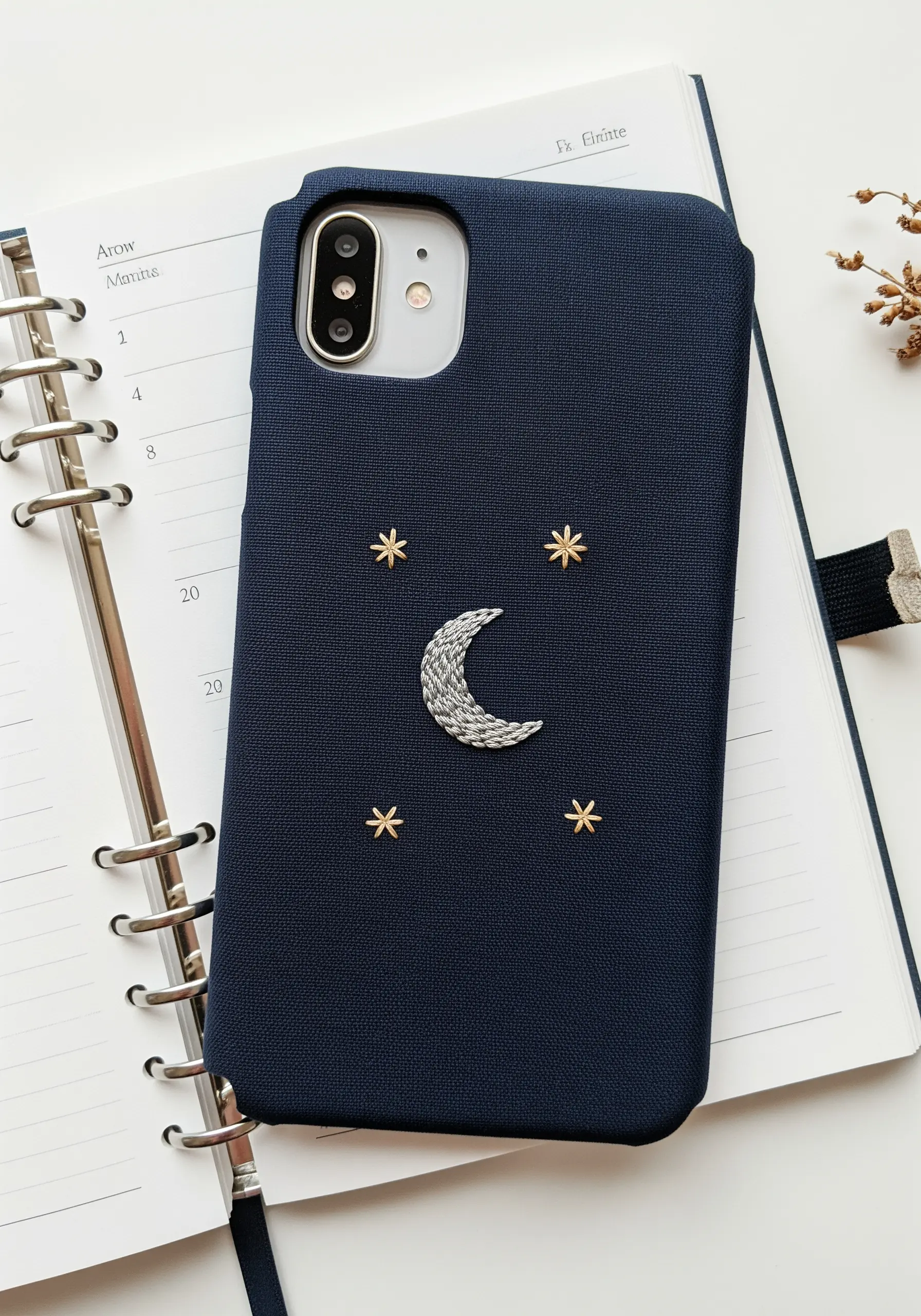 Embroidered crescent moon in silver metallic thread with small gold stars on a navy phone case.