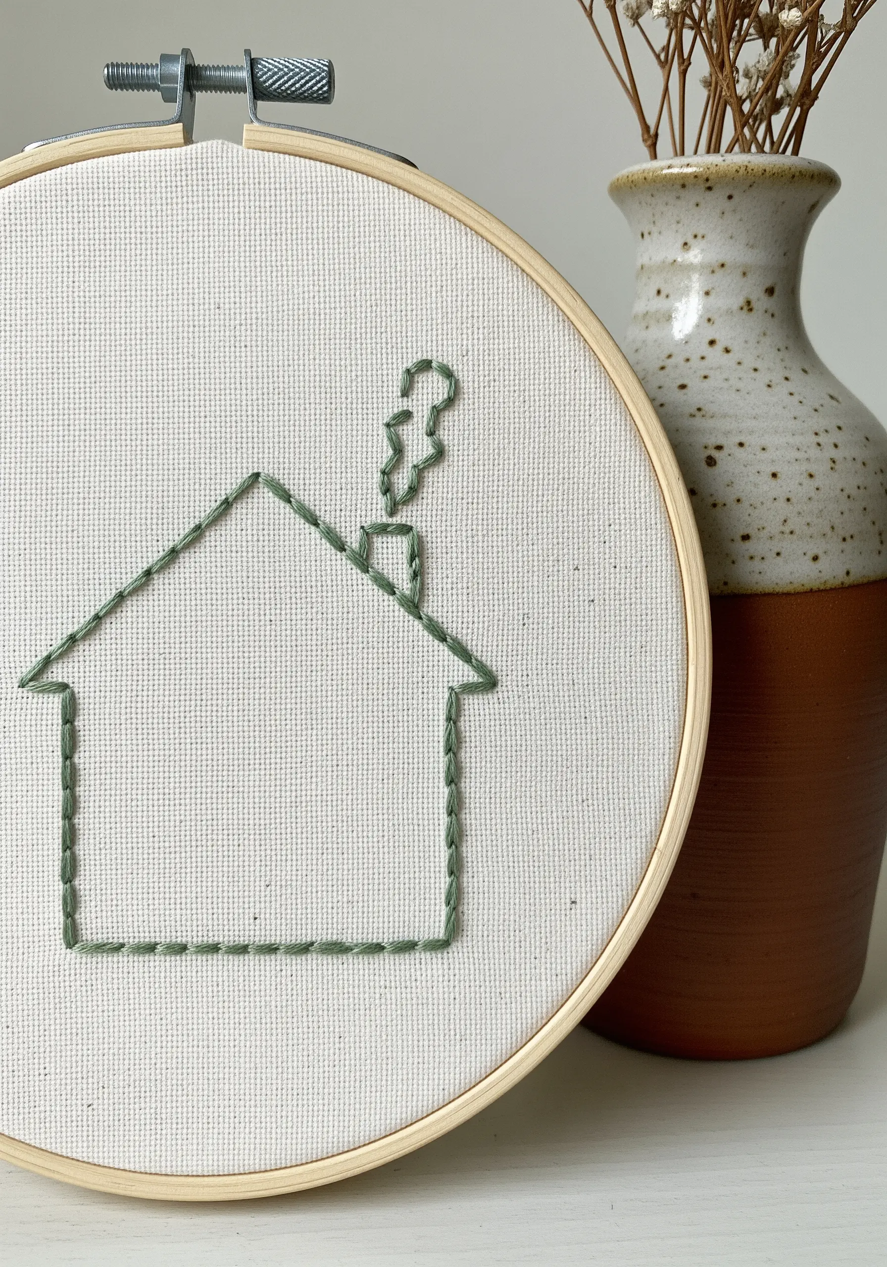 A simple outline of a house with smoke from the chimney, stitched in green.