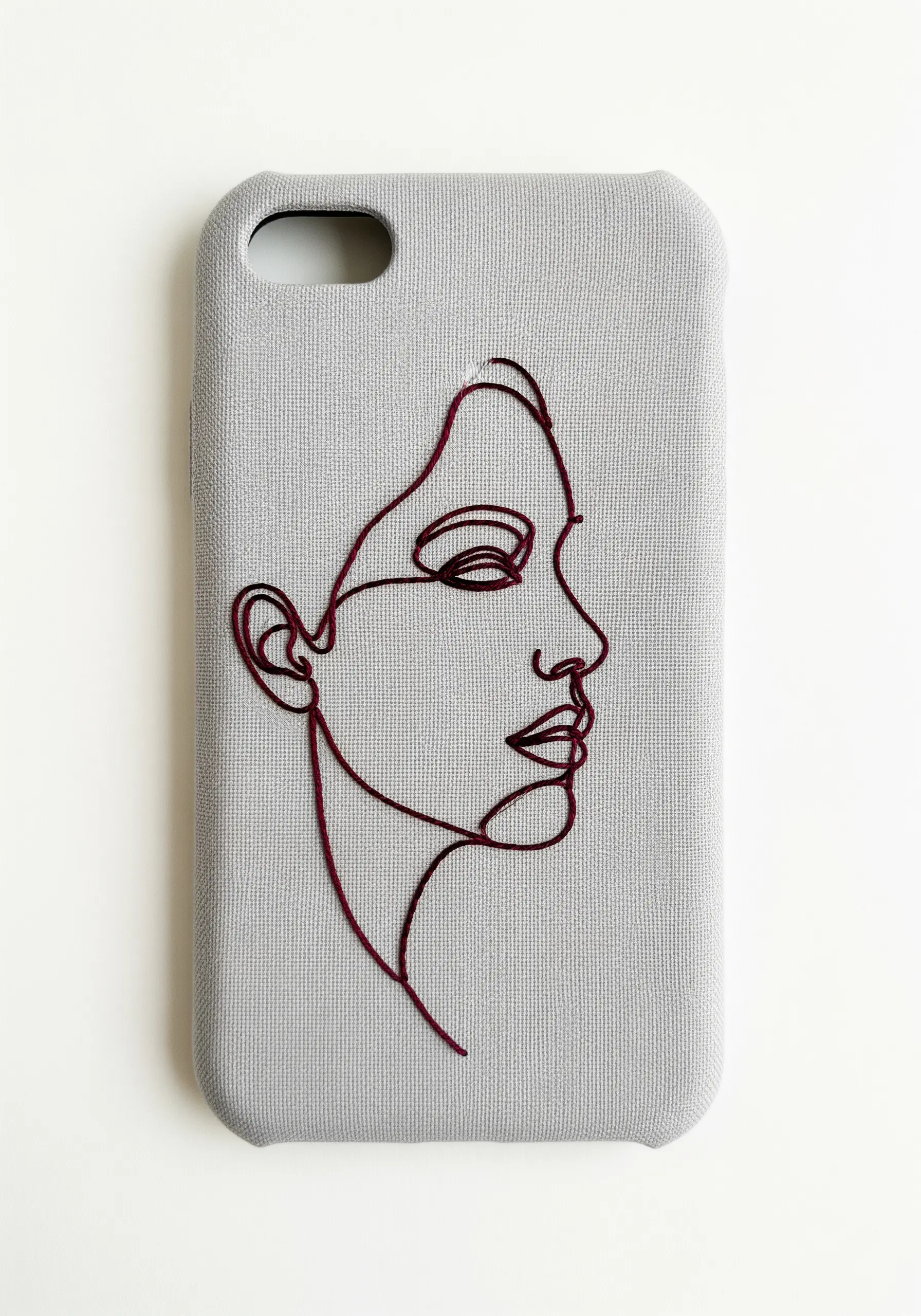 A modern line art portrait of a face, embroidered in a single continuous dark red line.