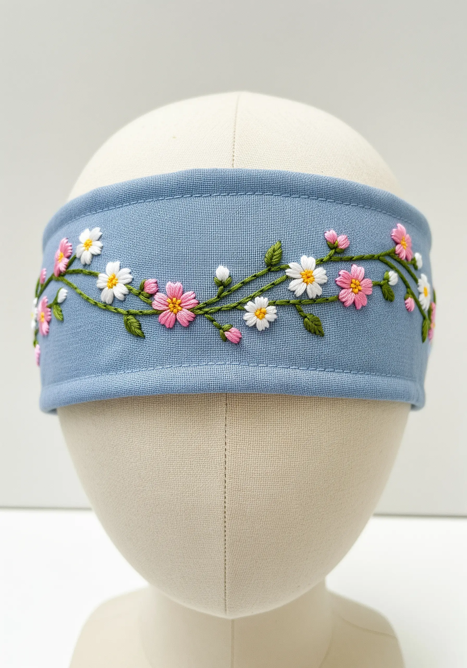 A trailing vine of cherry blossoms and daisies embroidered on a blue fabric headband.