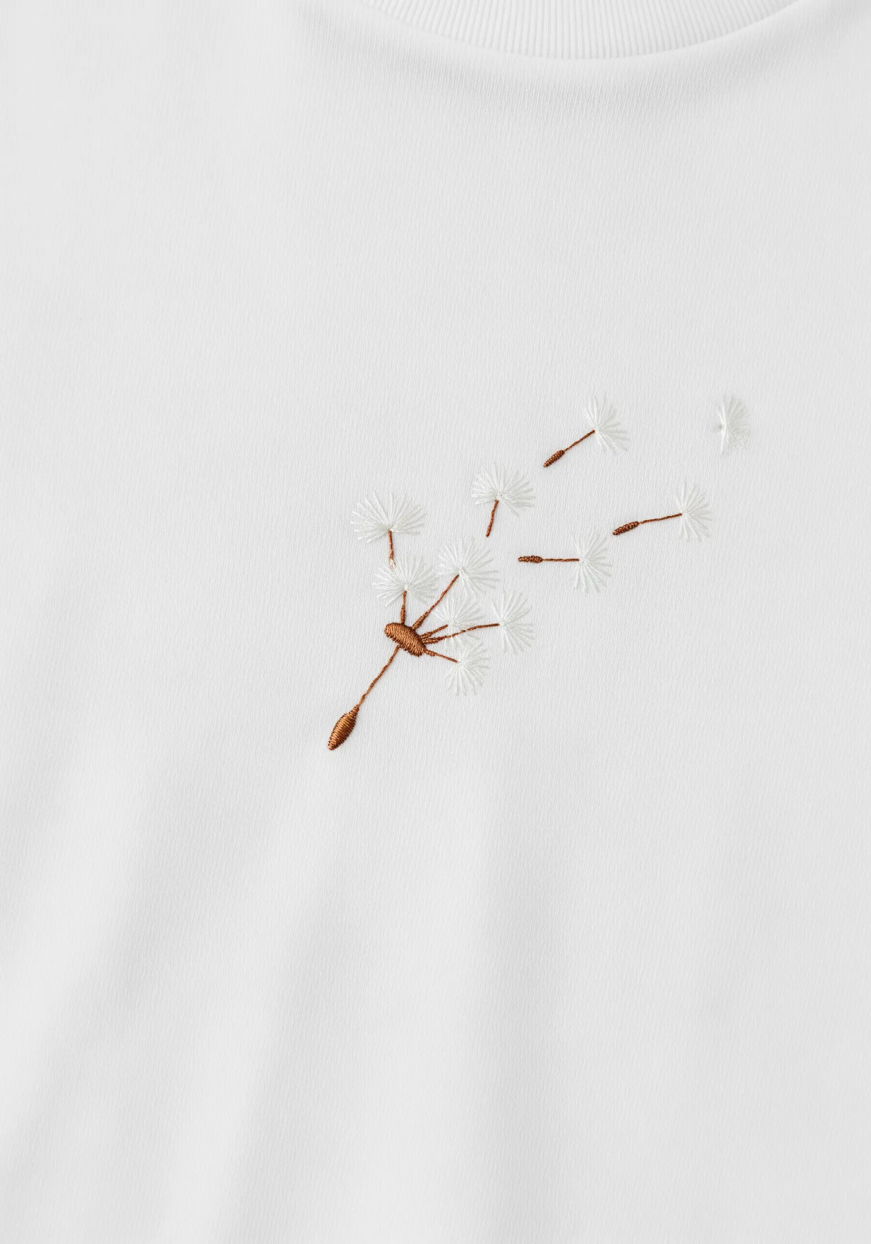 A dandelion with seeds blowing away, embroidered in brown and white thread.