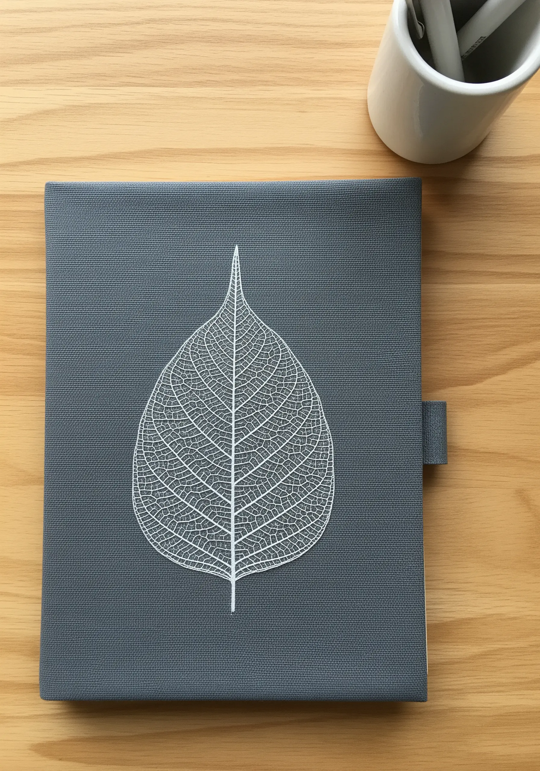 Ultra-fine white thread embroidery of a skeleton leaf on a grey book cover.