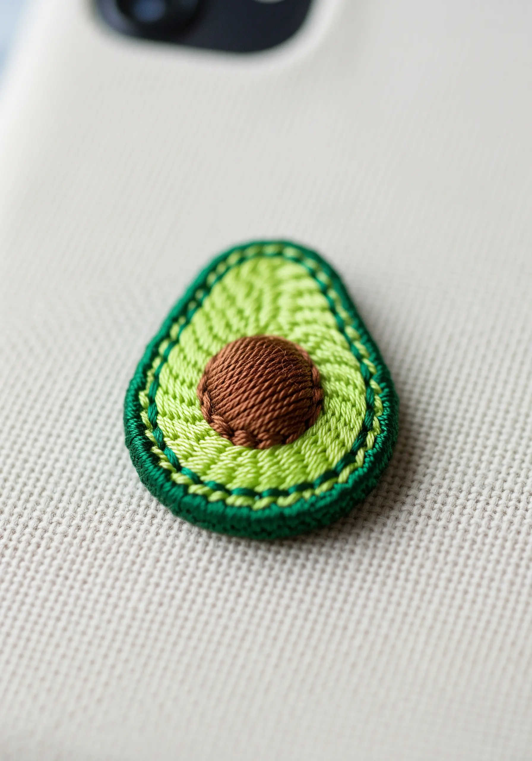A detailed, dimensional embroidery of a halved avocado with a central pit.