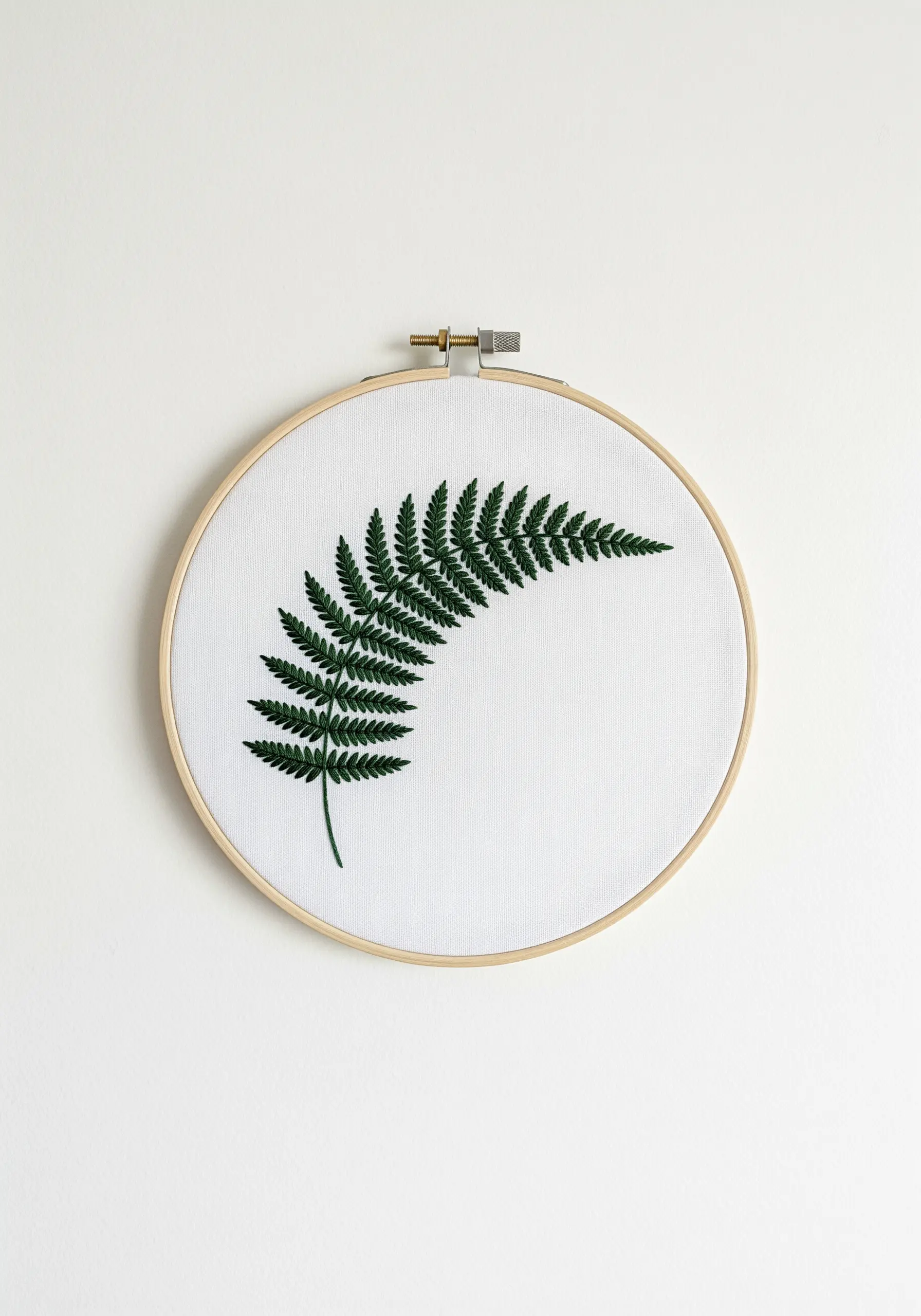 Minimalist embroidery of a single, dark green fern frond on white fabric.