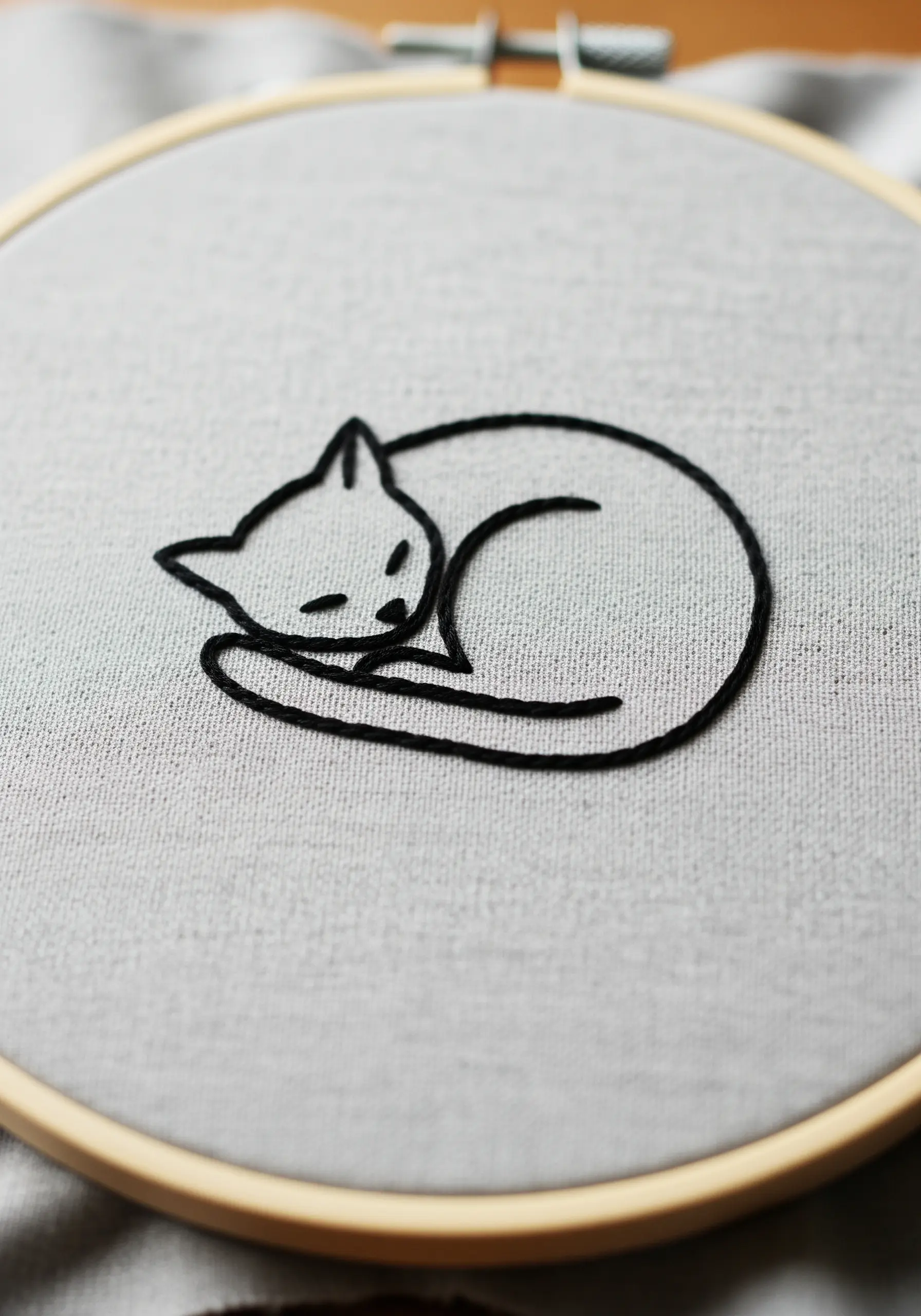 Minimalist line art embroidery of a sleeping cat curled into a circle.
