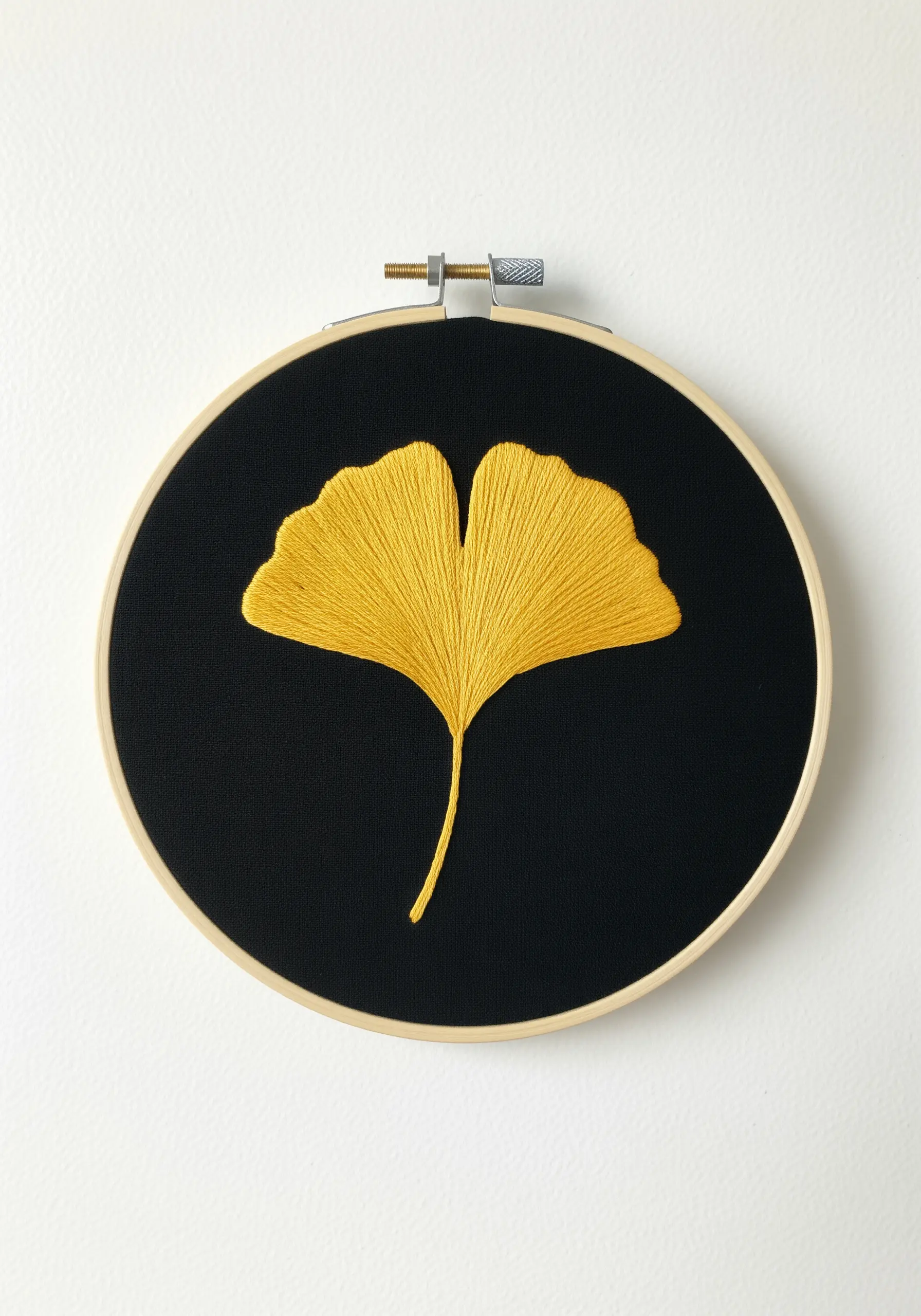 A single yellow ginkgo leaf embroidered with fanned satin stitch on black fabric.