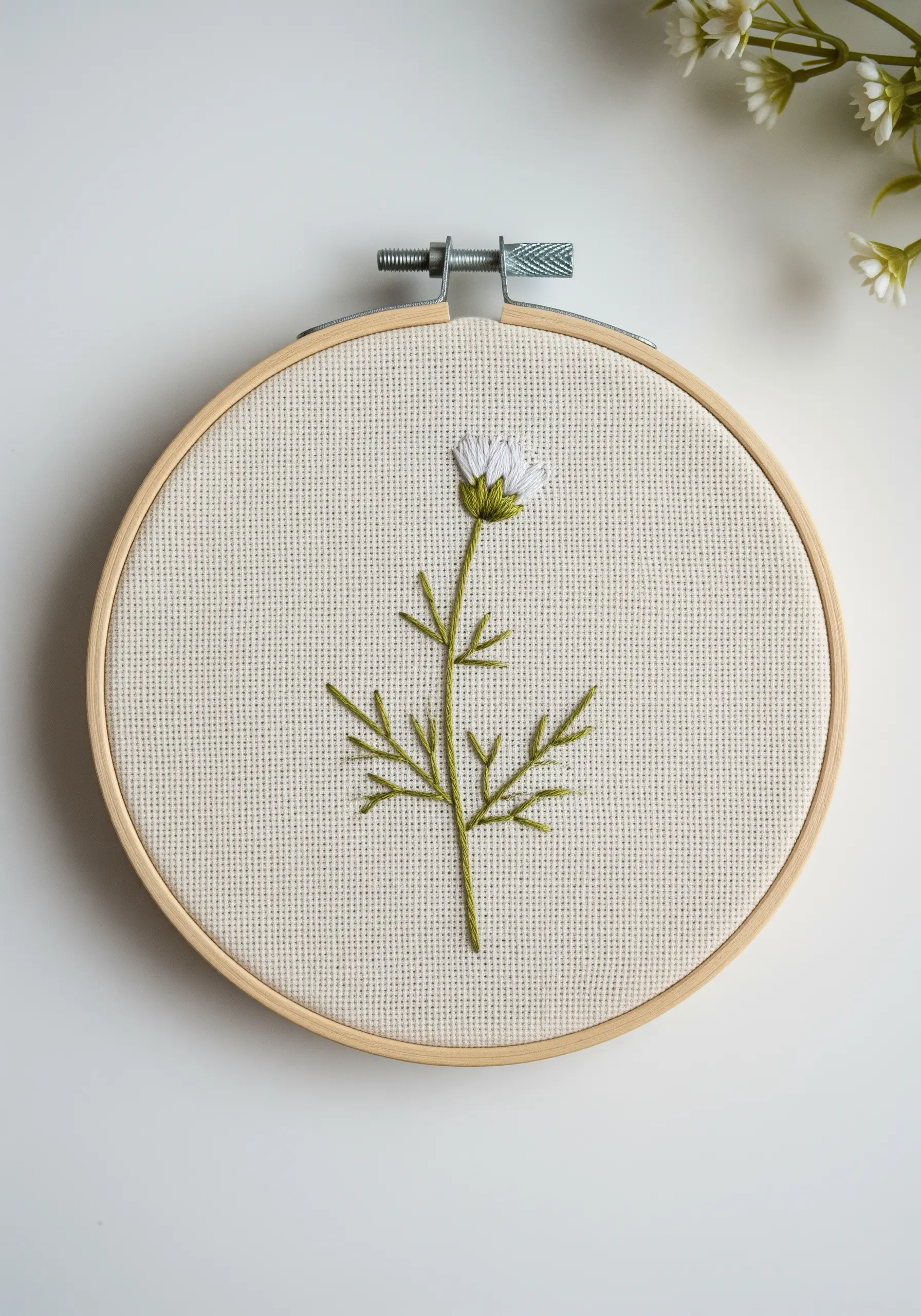 A single chamomile flower embroidered with delicate green and white stitches.
