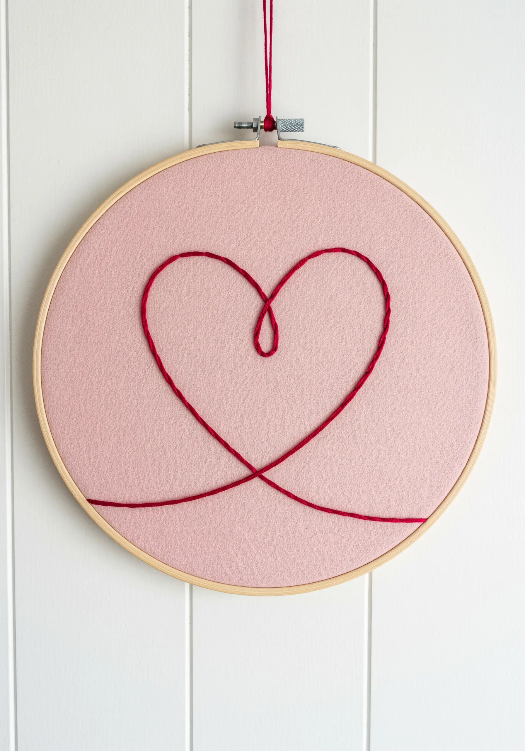 A simple heart drawn with a single, continuous red thread on a pink fabric background.