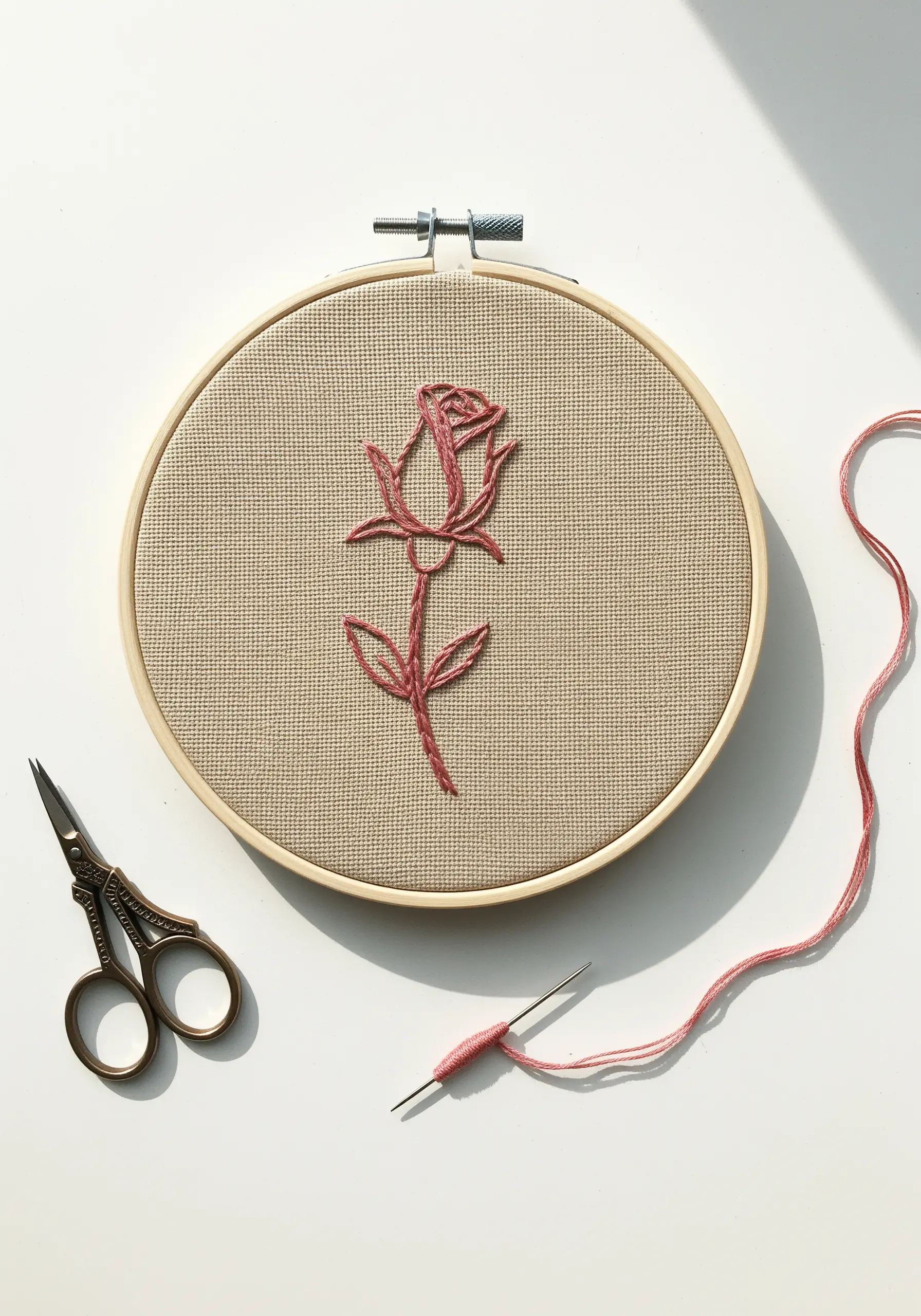A single rose embroidered in pink line art on a neutral, textured fabric.