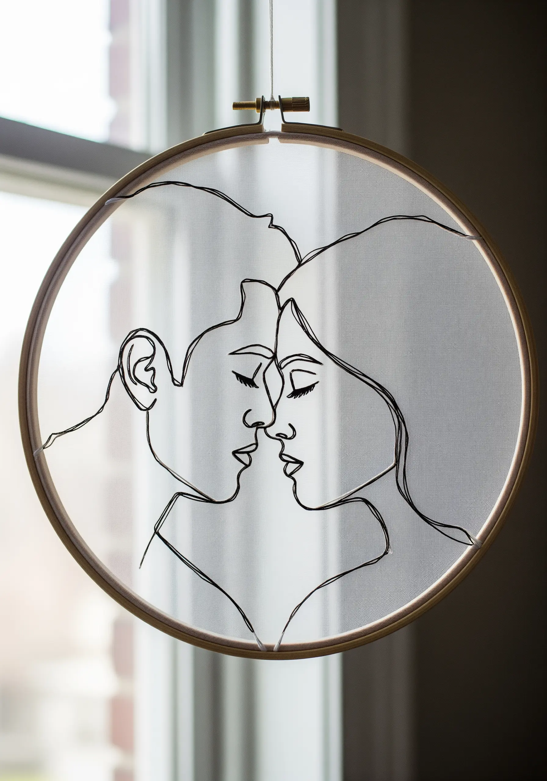 A minimal line art portrait of a couple stitched in black thread on transparent tulle fabric.