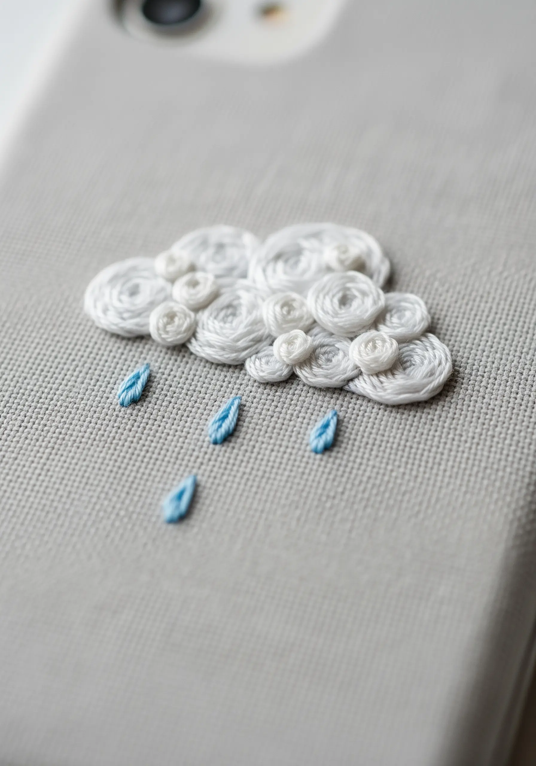 A fluffy, dimensional cloud made of woven wheel stitches with small blue raindrops.