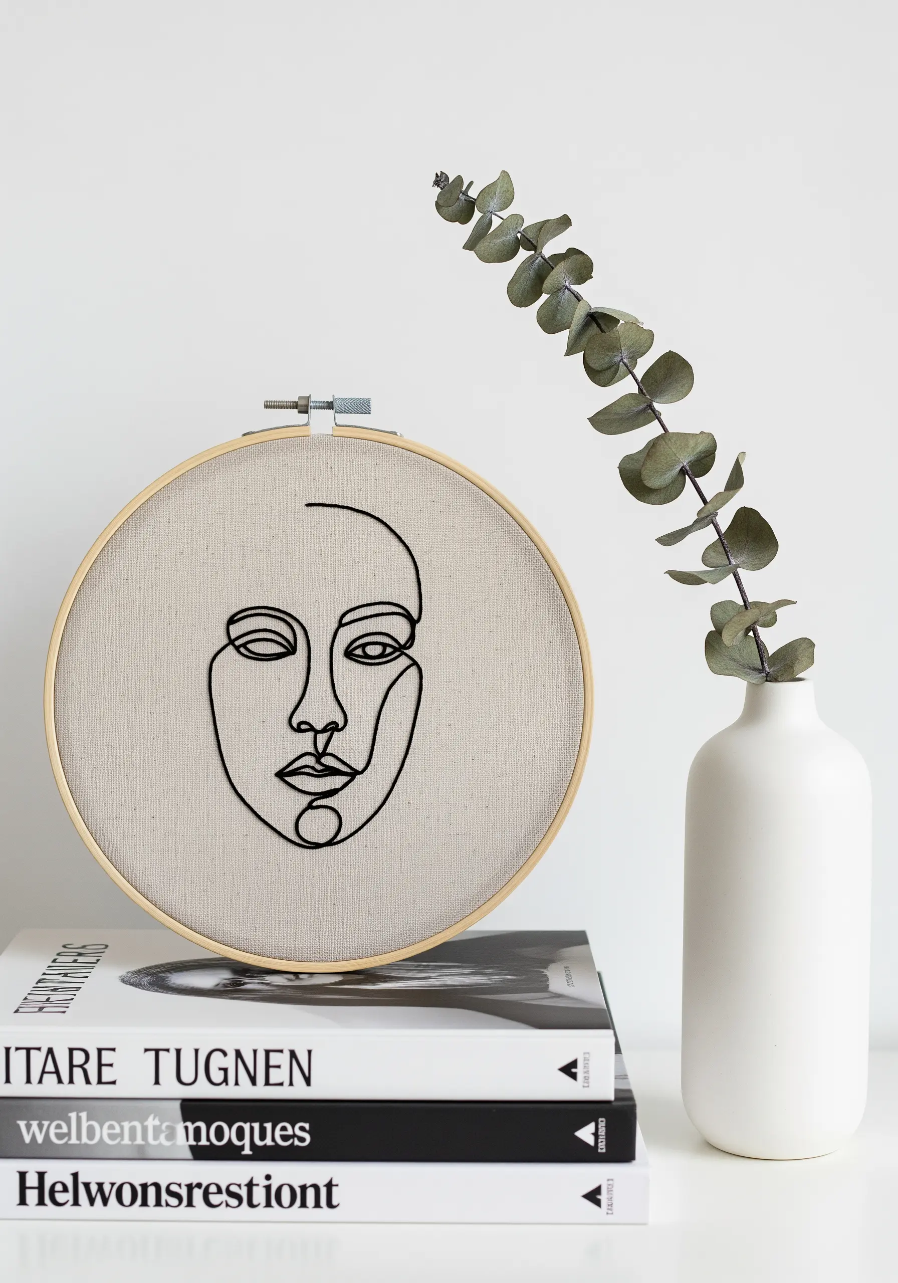 A minimalist, single-line art portrait of a face embroidered in black on a hoop.