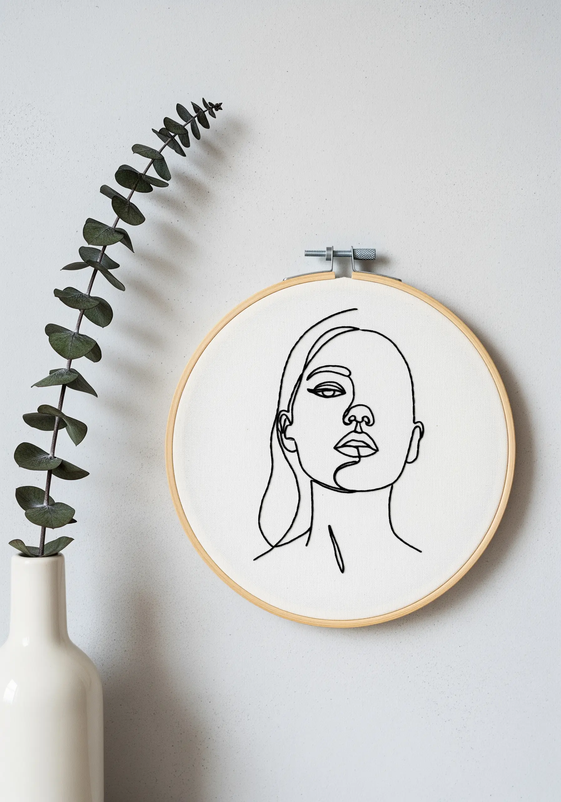Minimalist single-line portrait embroidered in black thread on white fabric.
