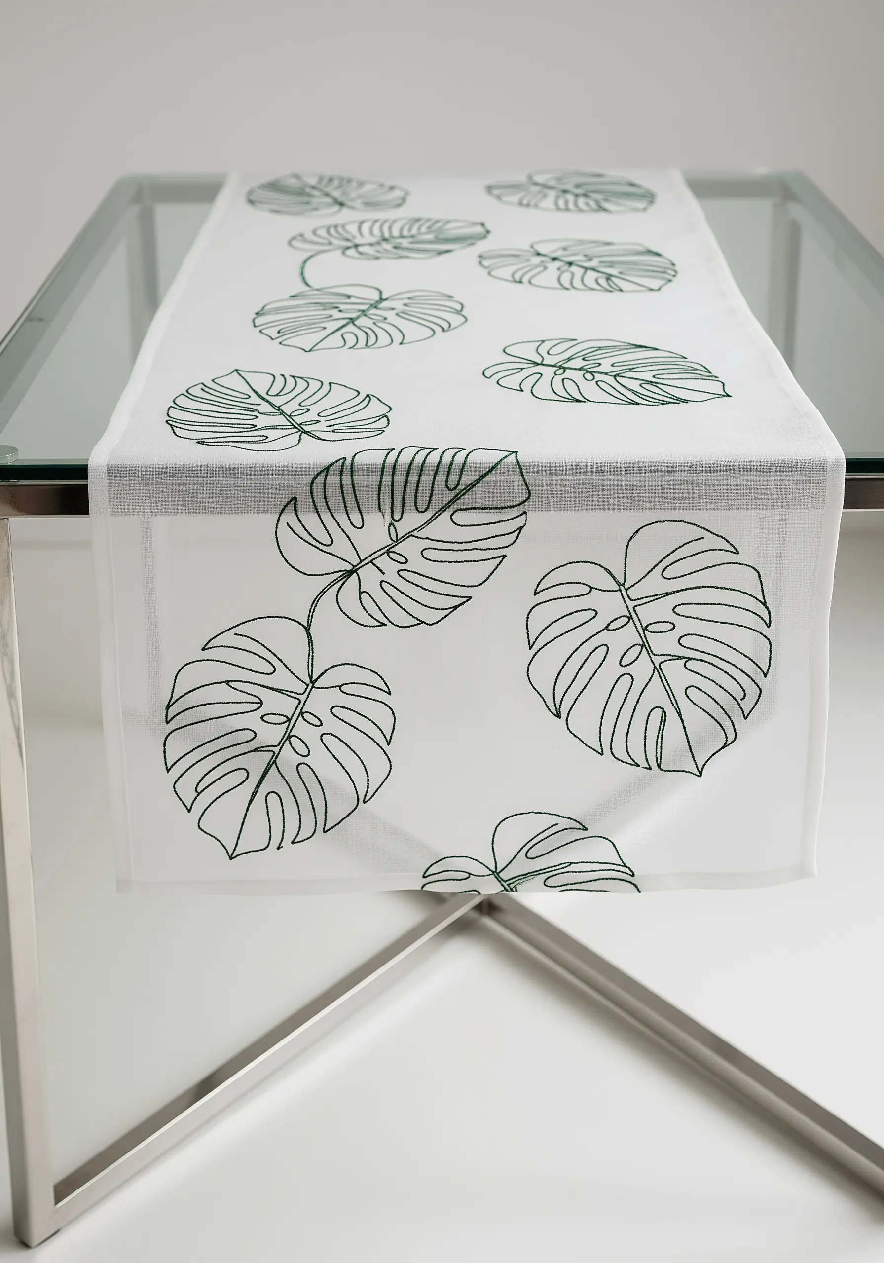 White table runner with green outline embroidery of monstera leaves.