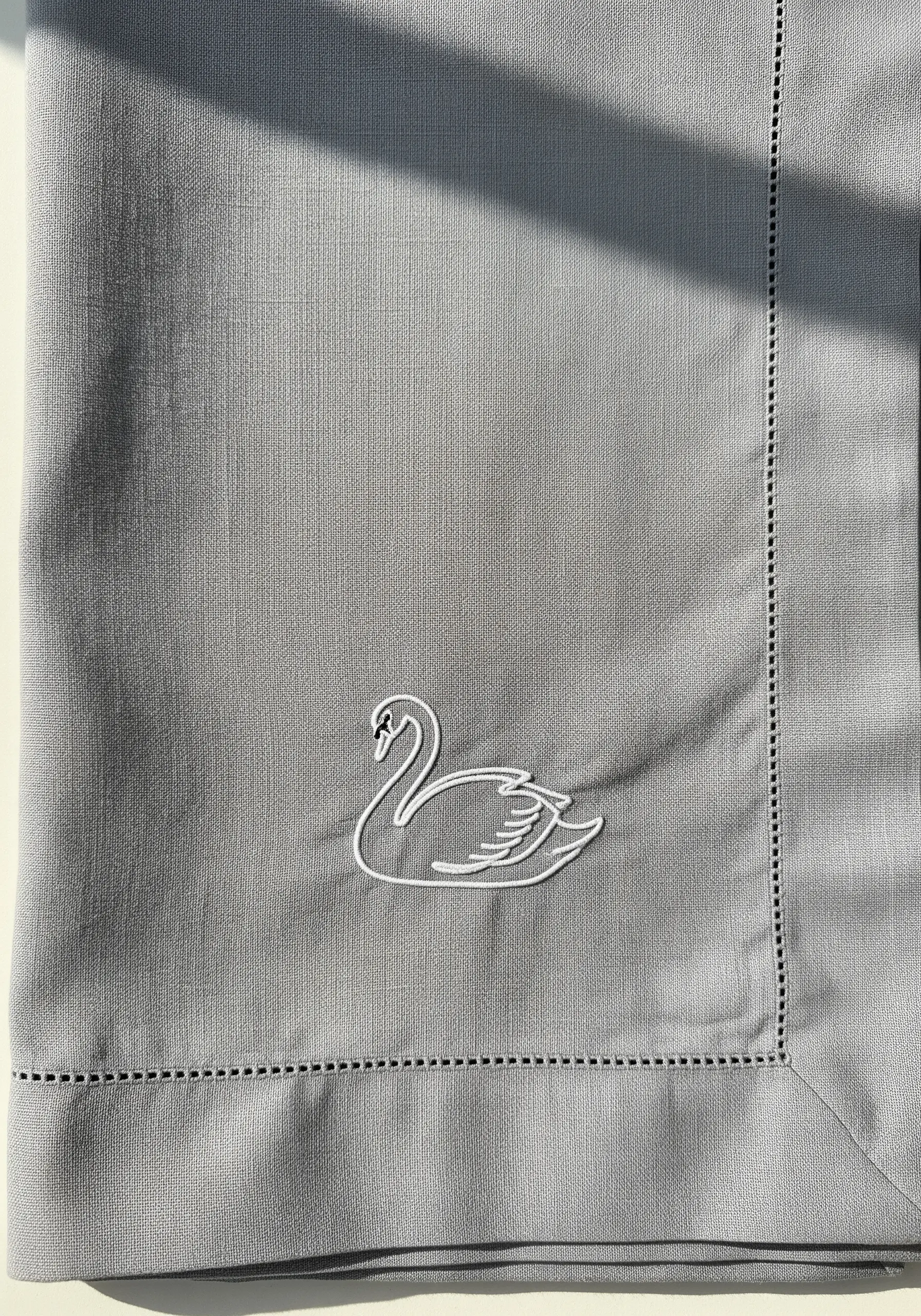 A graceful swan embroidered in white thread on the corner of a grey linen napkin.