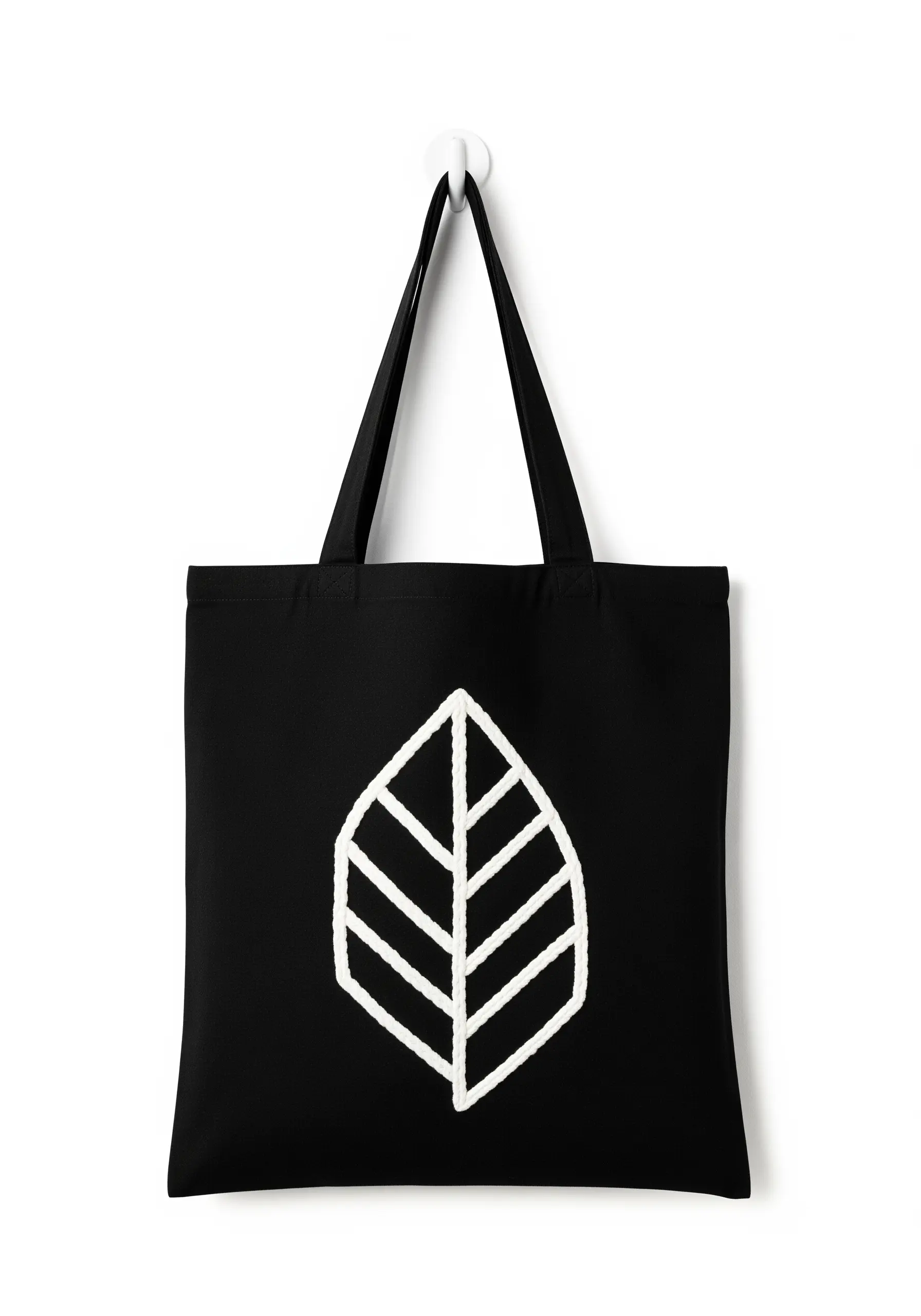 A bold, geometric leaf logo embroidered in thick white cord on a black canvas tote bag.