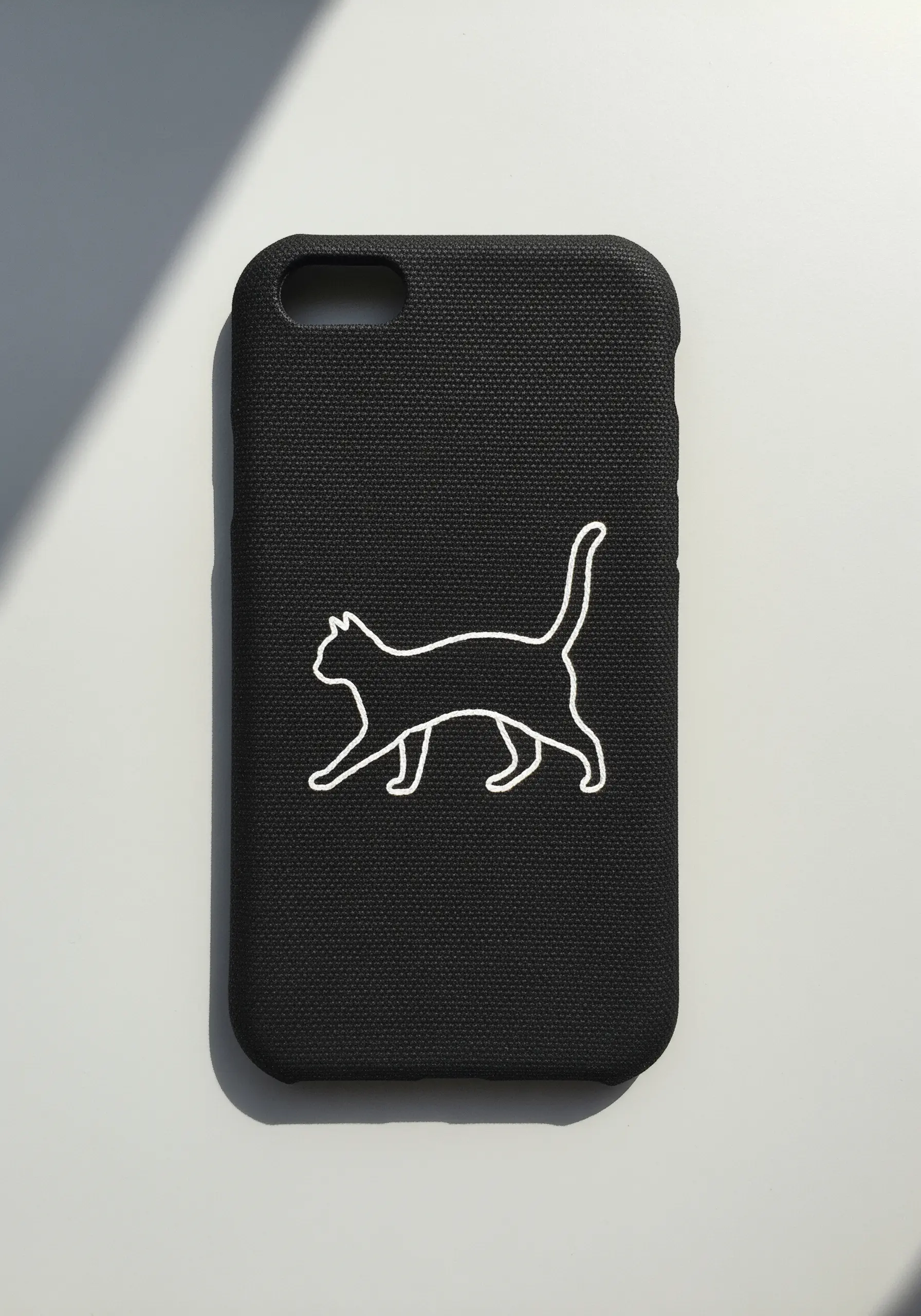 A minimalist white outline of a walking cat embroidered on a black phone case.