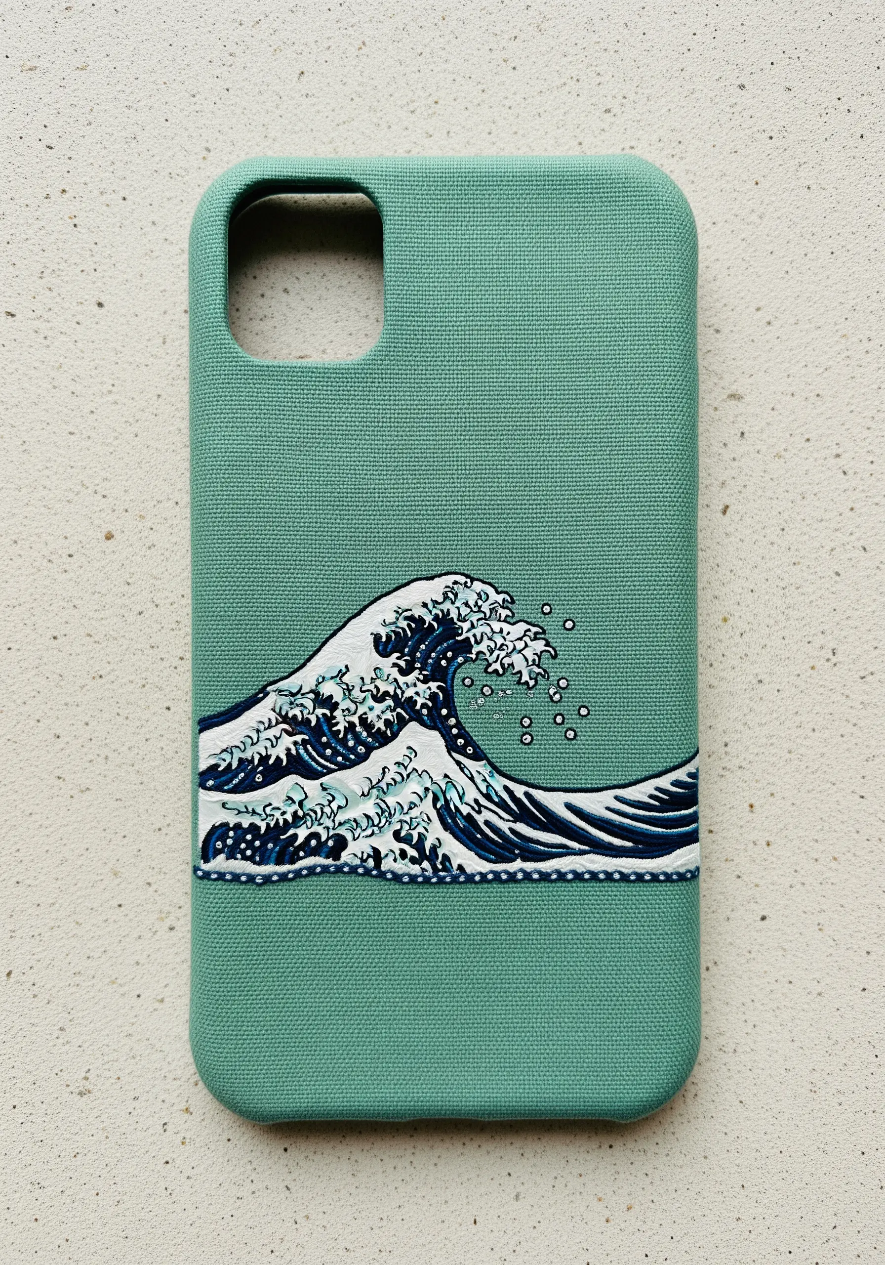 A detailed embroidery of 'The Great Wave off Kanagawa' on a teal phone case.