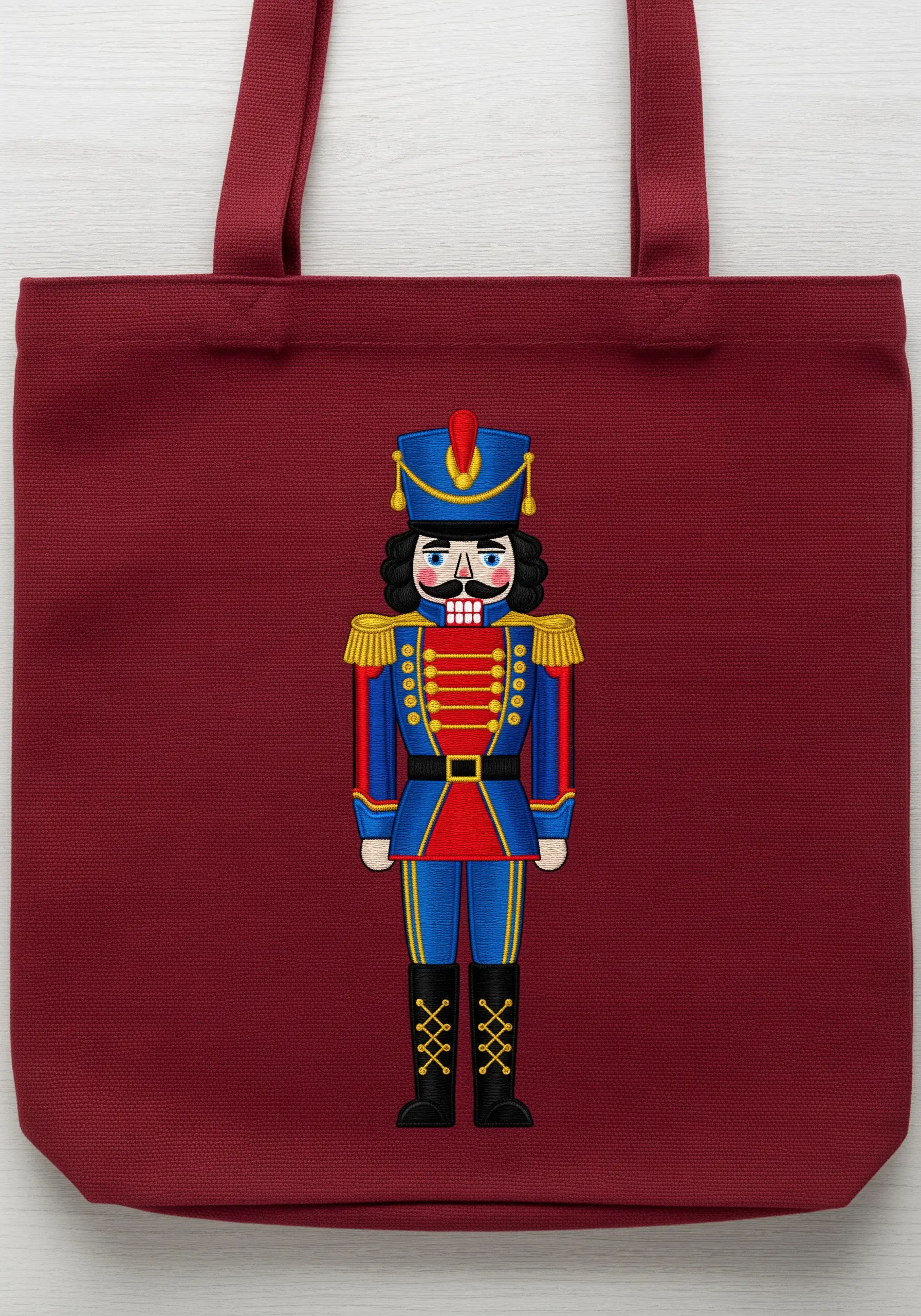 A detailed embroidered nutcracker soldier in a red and blue uniform on a burgundy tote bag.