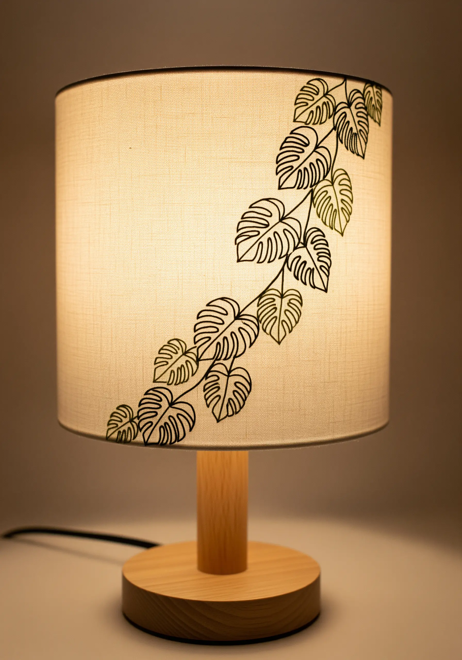 A climbing monstera vine embroidered in black outline on a cylindrical fabric lampshade.