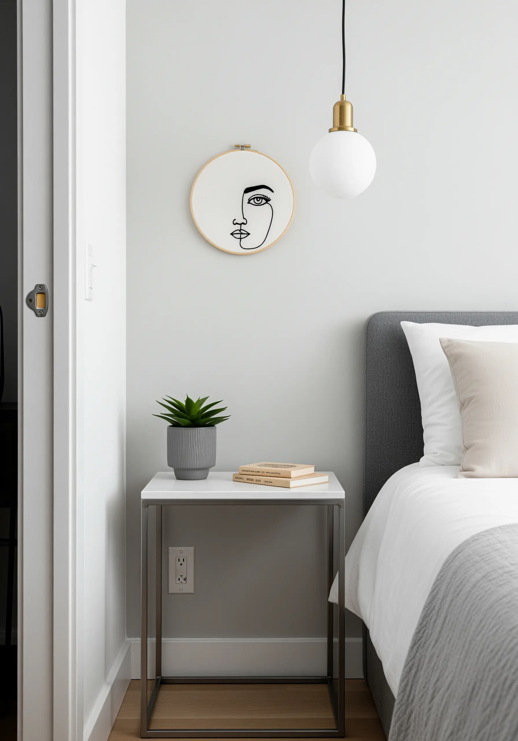 A small embroidery hoop with a minimalist single-line art face, hanging on a grey wall.